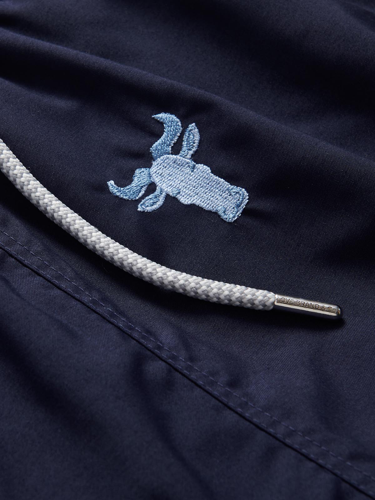 Navy blue men's swim shorts with intricate sky blue embroidered wildebeest design and white drawstring detail.