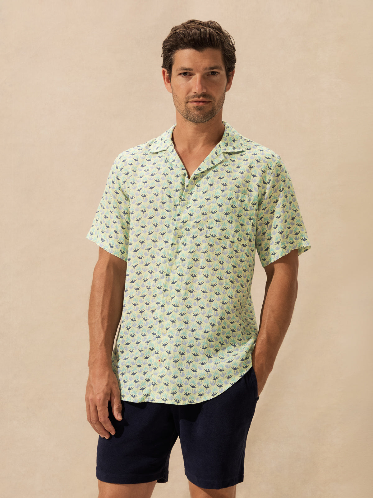 A man wearing a light green short-sleeve button-up shirt with a small repeating tropical leaf pattern.