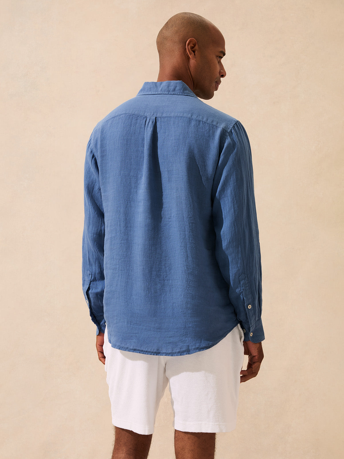 Man wearing a blue linen shirt and white shorts on a beige background