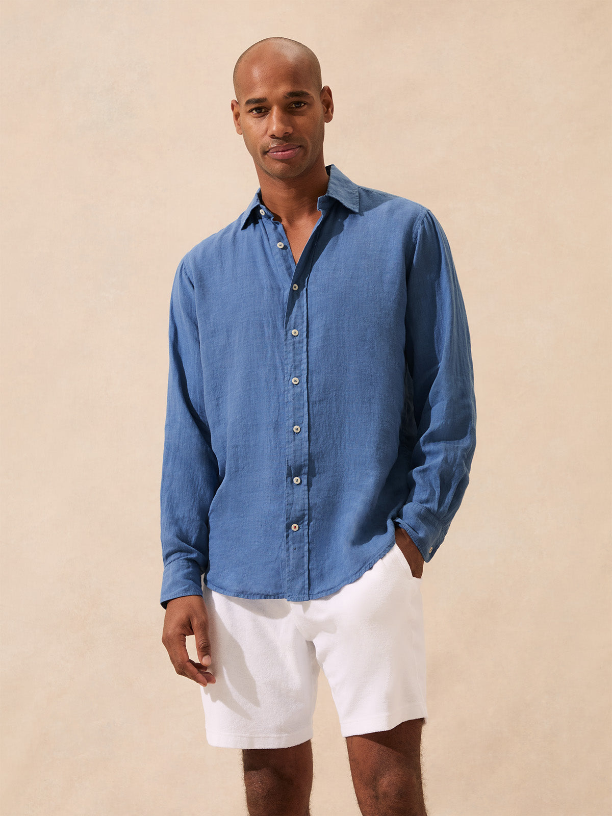 Man wearing a blue button-up shirt and white shorts against a beige background