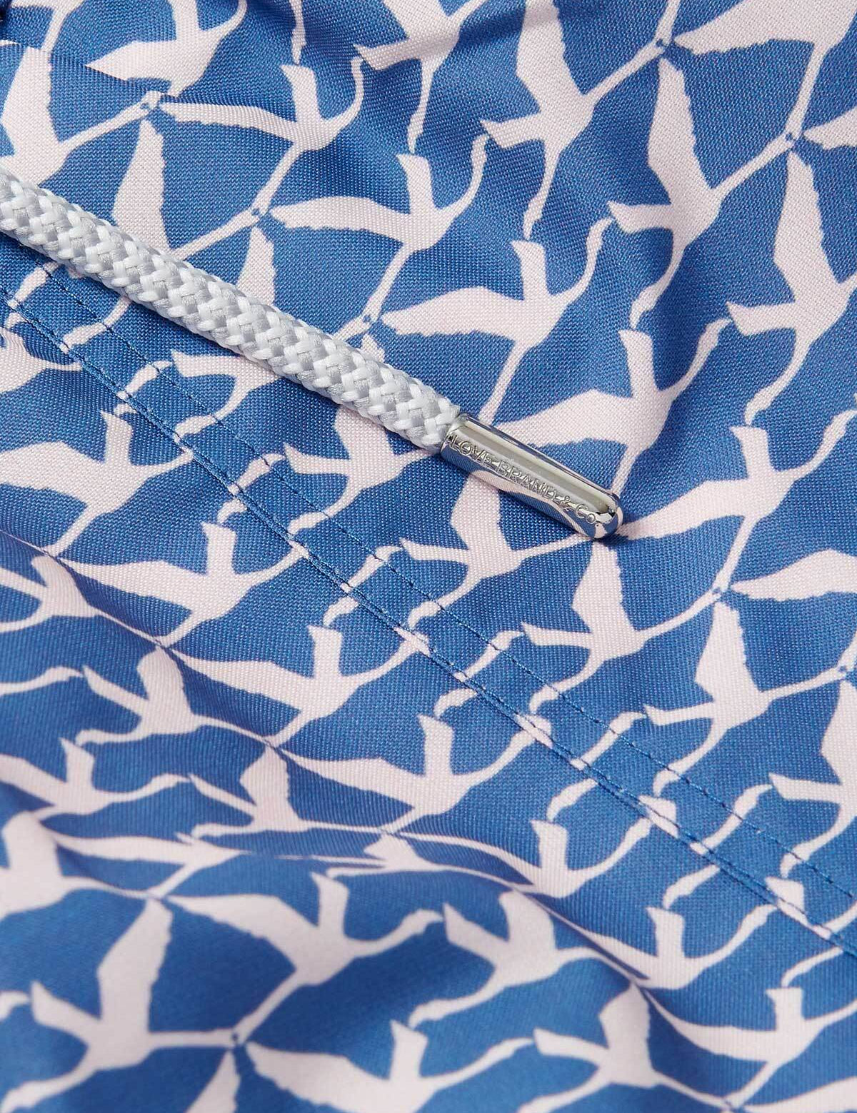 Close-up view of Men's Flamingo Flamboyance Staniel Swim Shorts featuring blue fabric with a white flamingo pattern and a drawstring with silver metal tips.