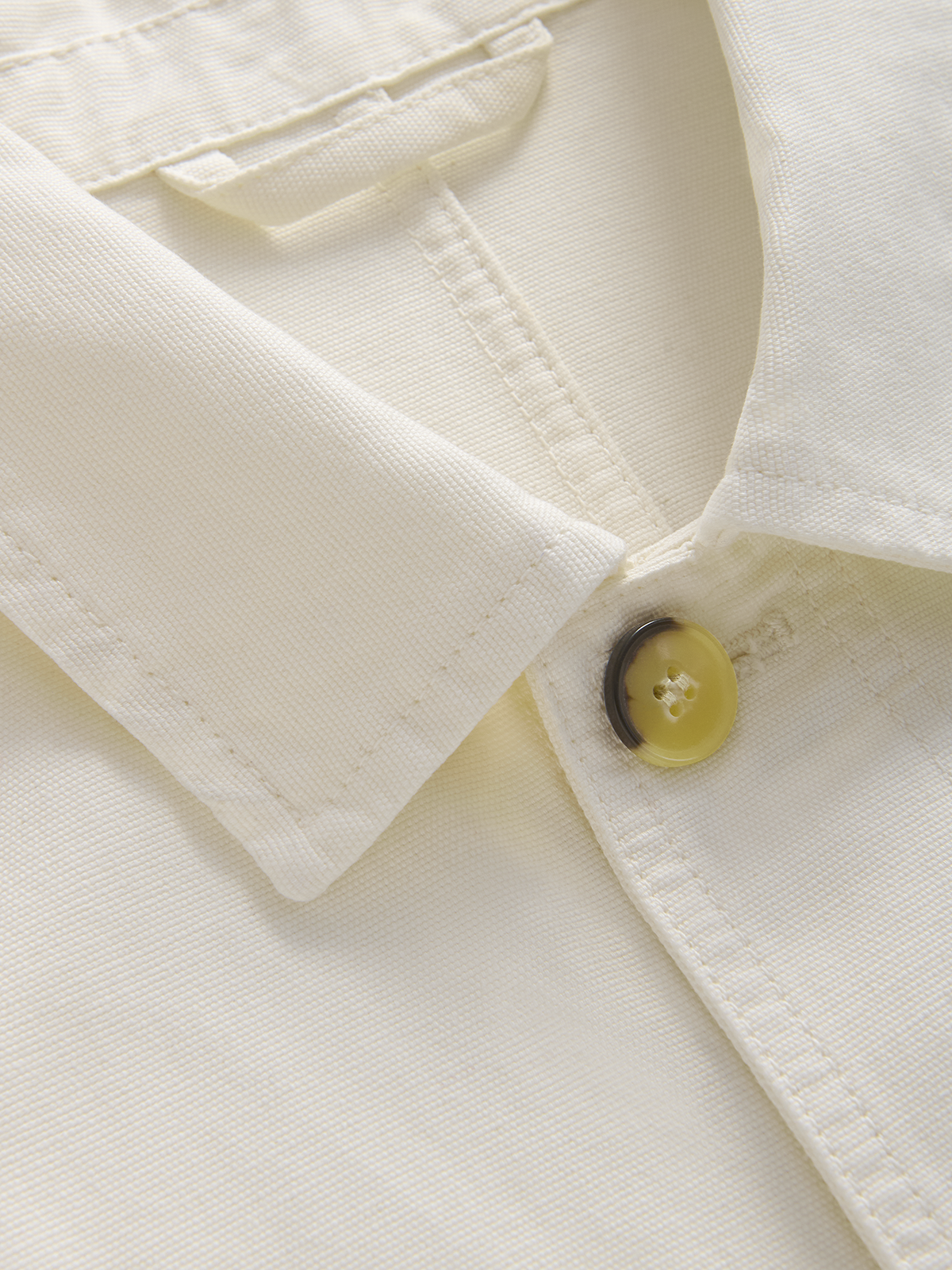 Close-up of a cream-colored jacket collar with a single yellow button, showing the fabric texture and stitching details.
