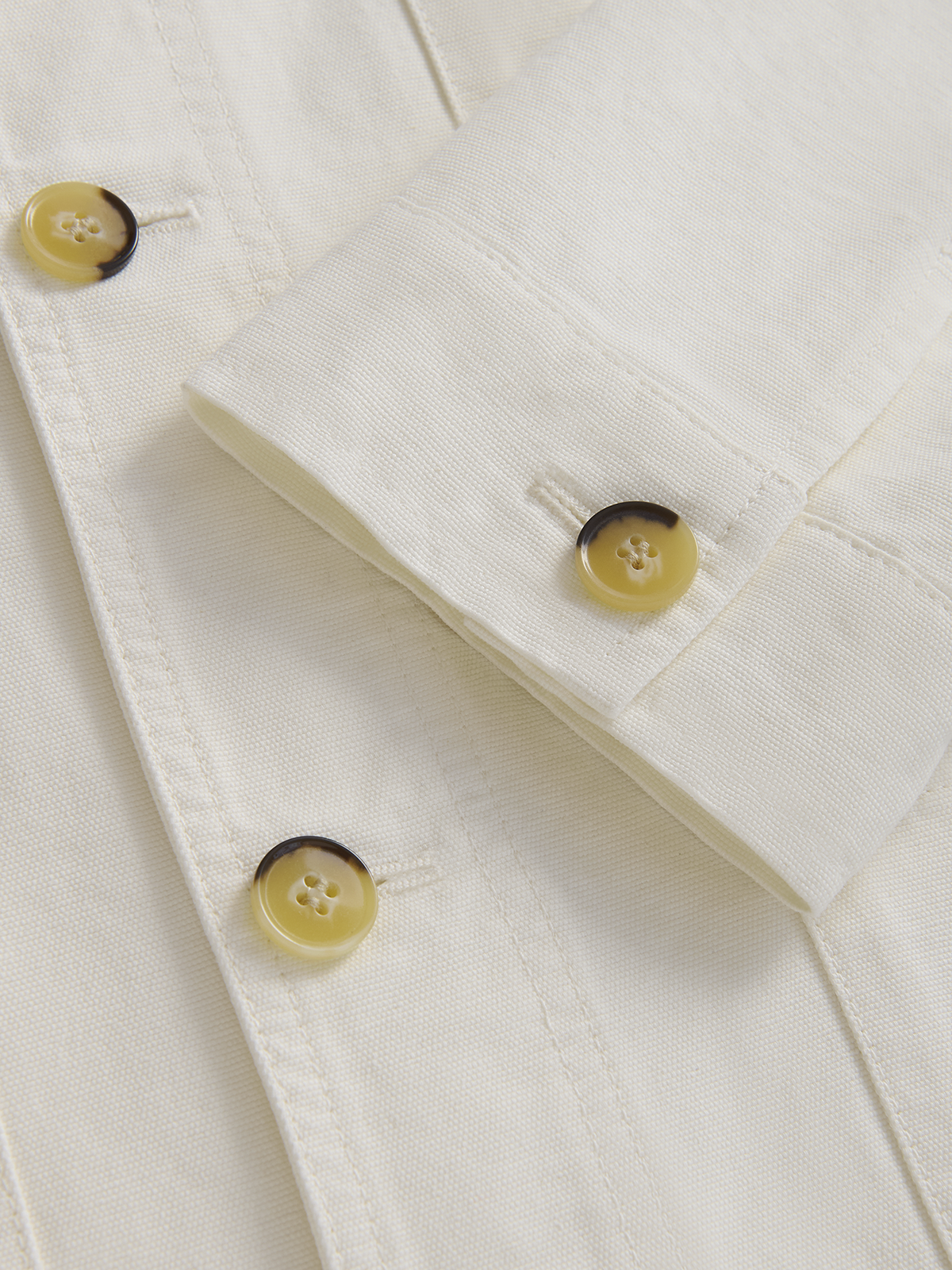 Close-up of a cream-coloured cotton jacket with yellow tortoiseshell buttons on the cuff and front placket.