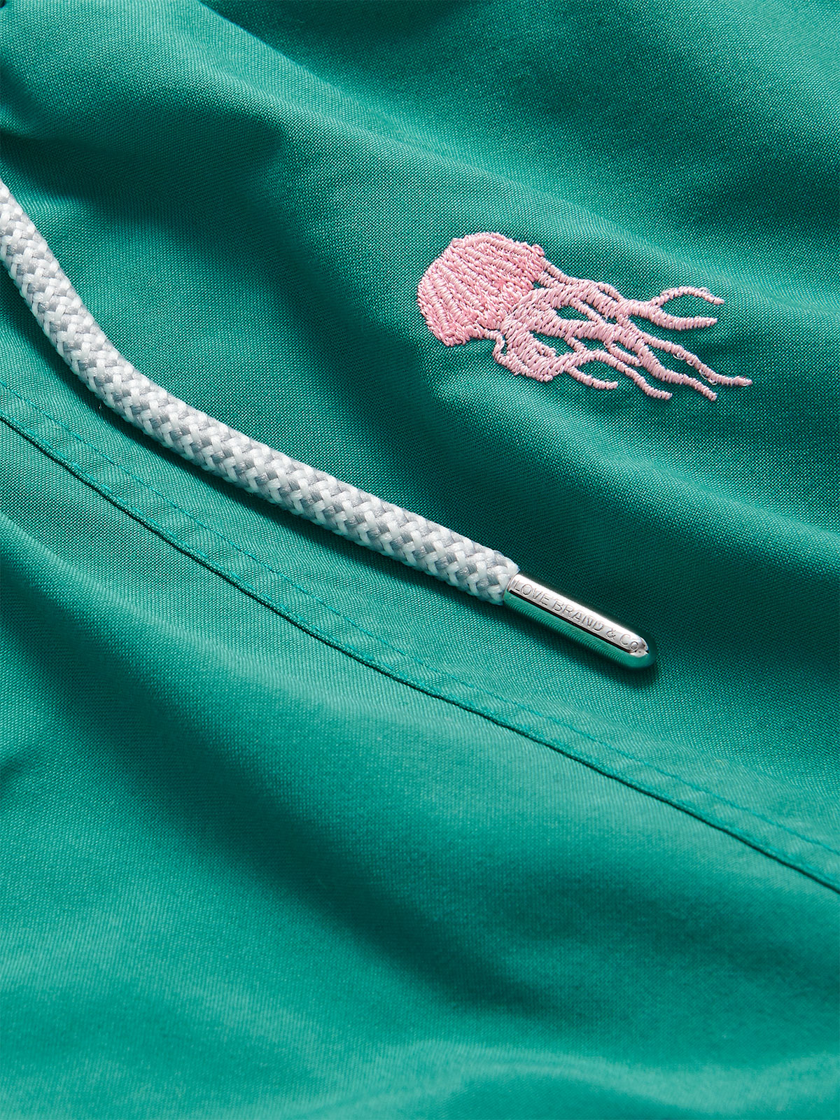 Palm Green boys' swim shorts with pink embroidered jellyfish motif and braided white drawstring.