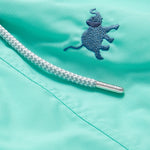 Close-up image of Boys Elephants Galore Staniel swim shorts in Cay Green, featuring a blue embroidered elephant and white braided drawstring.