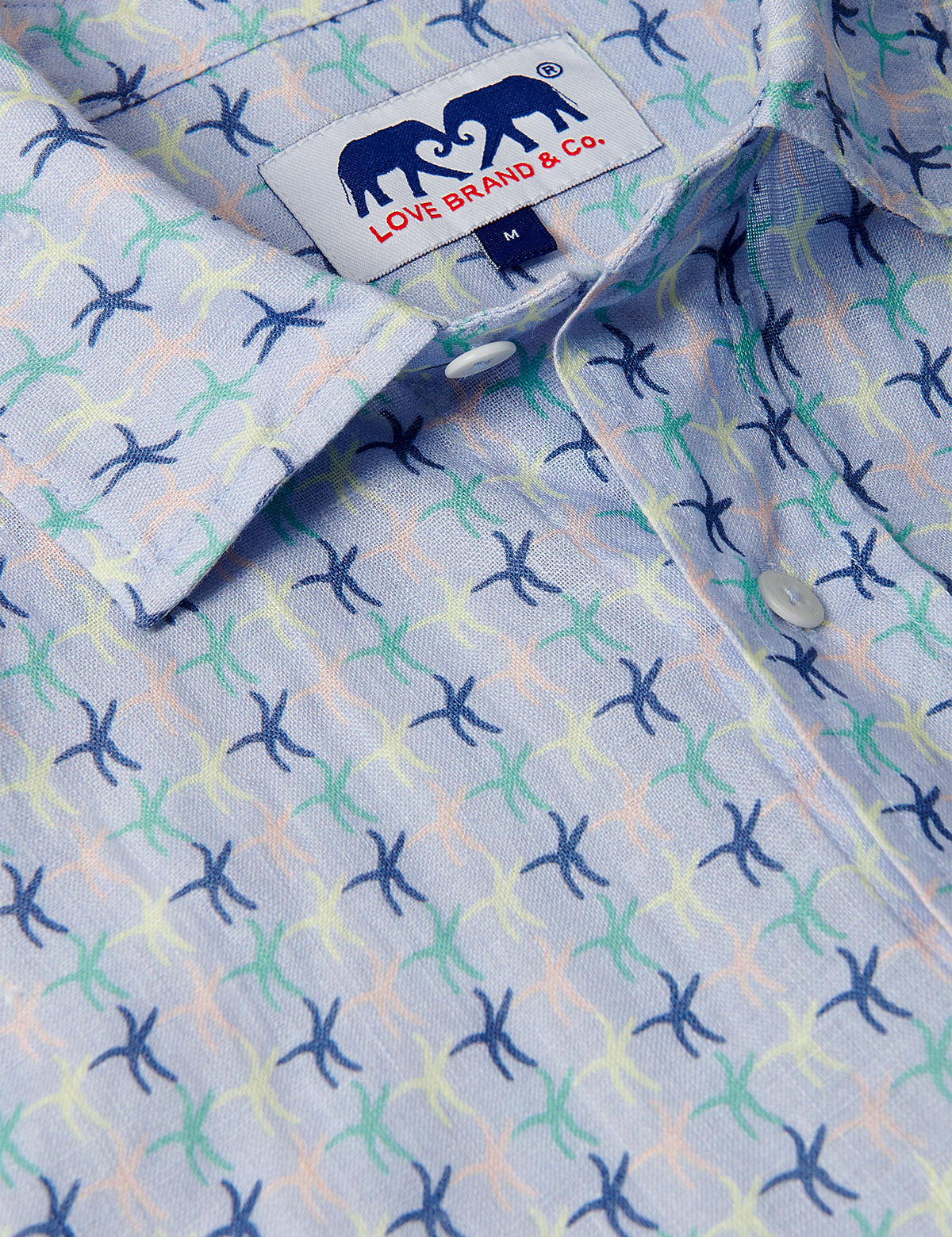 Close-up of Men's Star Dancer Abaco Linen Shirt with pastel pink, limoncello, cay green, and deep blue sea star motifs on an ocean blue background.