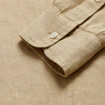 Detailed view of Men's Coconut Windermere Linen Long Sleeve Hoodie. Brown linen shirt with a drawstring hood. Crafted from 100% linen with half-button-up design and 2 large front pockets.