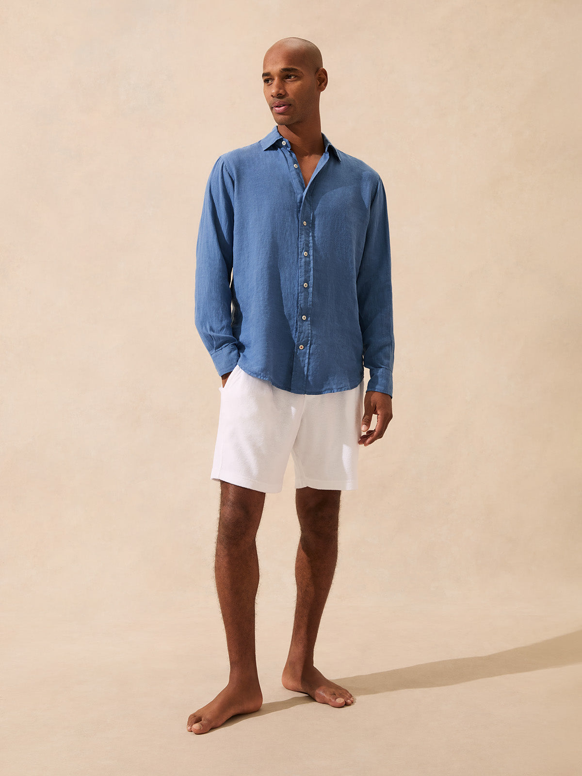 Man wearing a blue linen shirt and white shorts on a beige background