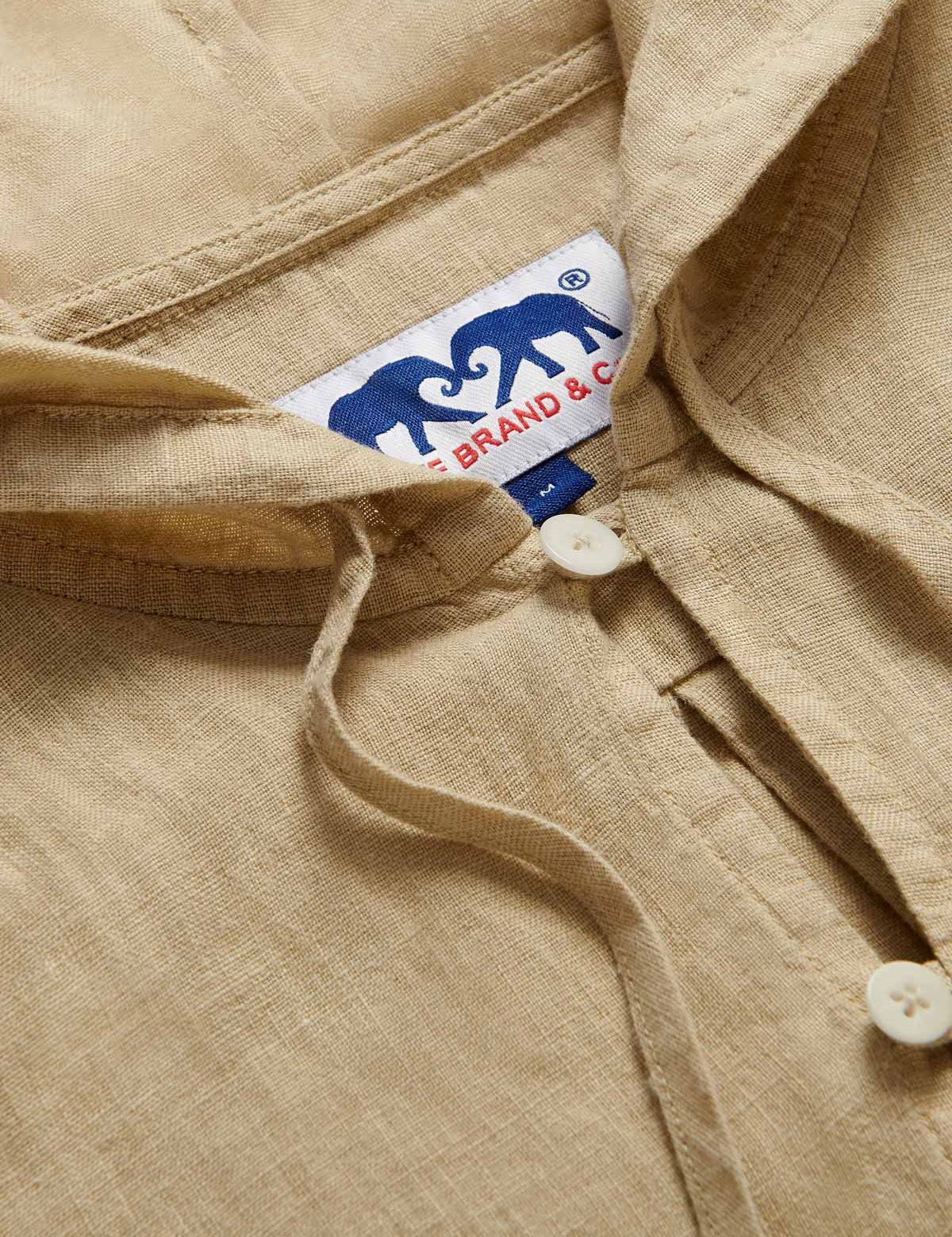 Close-up view of Men's Coconut Windermere Linen Long Sleeve Hoodie. Brown linen shirt with a drawstring hood. Crafted from 100% linen with half-button-up design and 2 large front pockets.