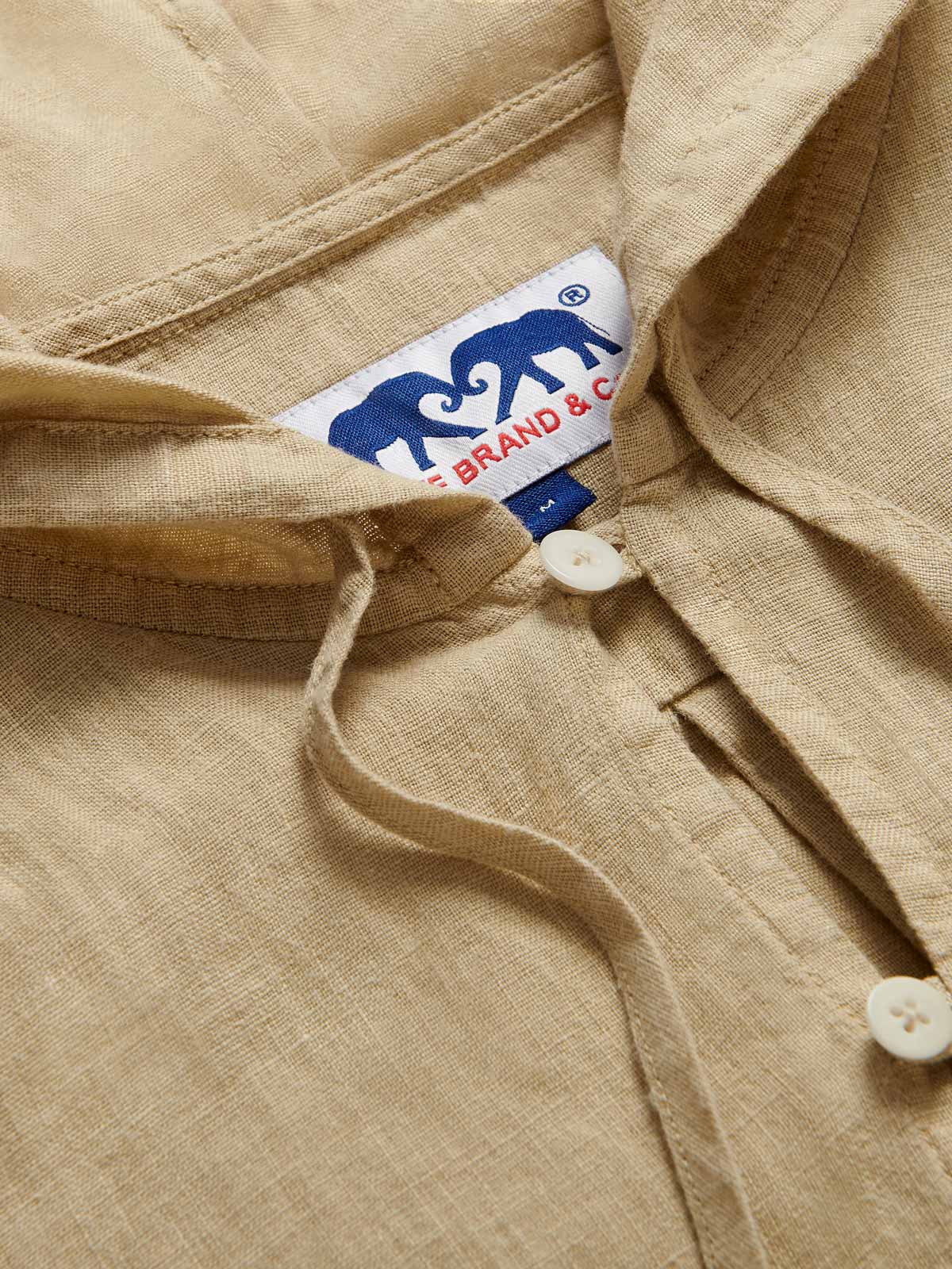 Close-up view of Men's Coconut Windermere Linen Long Sleeve Hoodie. Brown linen shirt with a drawstring hood. Crafted from 100% linen with half-button-up design and 2 large front pockets.