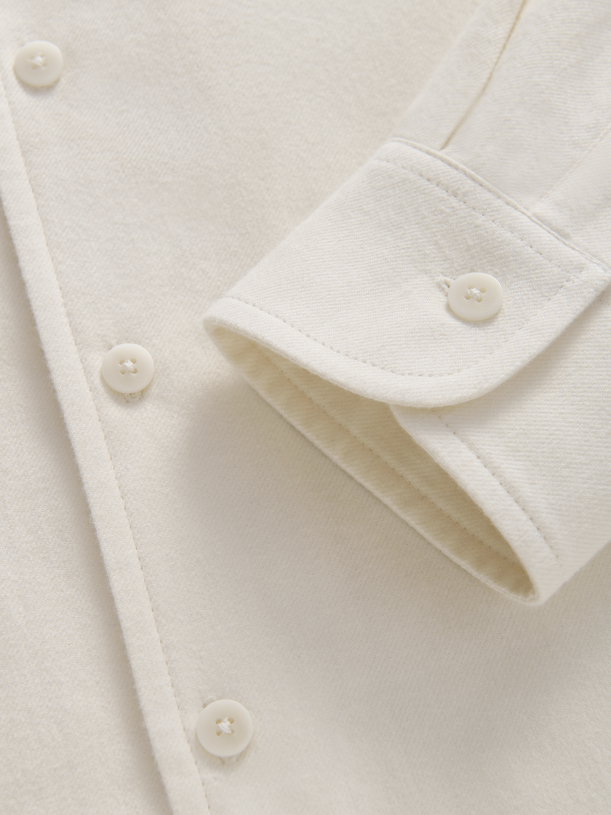 Close-up of an off-white or cream-colored button-down shirt showing the fabric texture, button details, and a folded cuff.