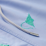 Close-up view of boys' swim shorts featuring vibrant turquoise manta ray embroidery on a pastel blue quick-dry fabric, with a detailed braided drawstring.