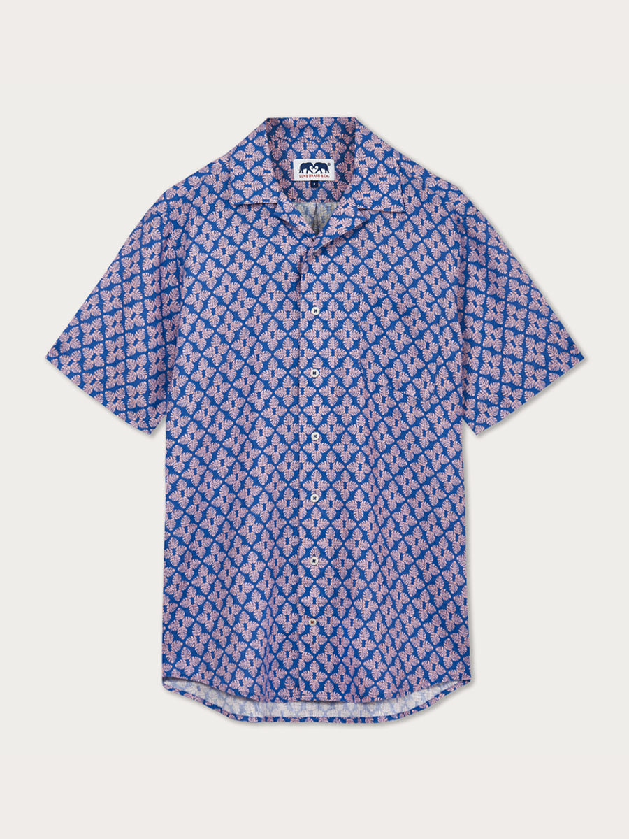 Men's Palm Paradise Arawak Linen Shirt with Monstera leaf print in pastel pink on blue. Men's linen shirt featuring short sleeves and corozo nut buttons.