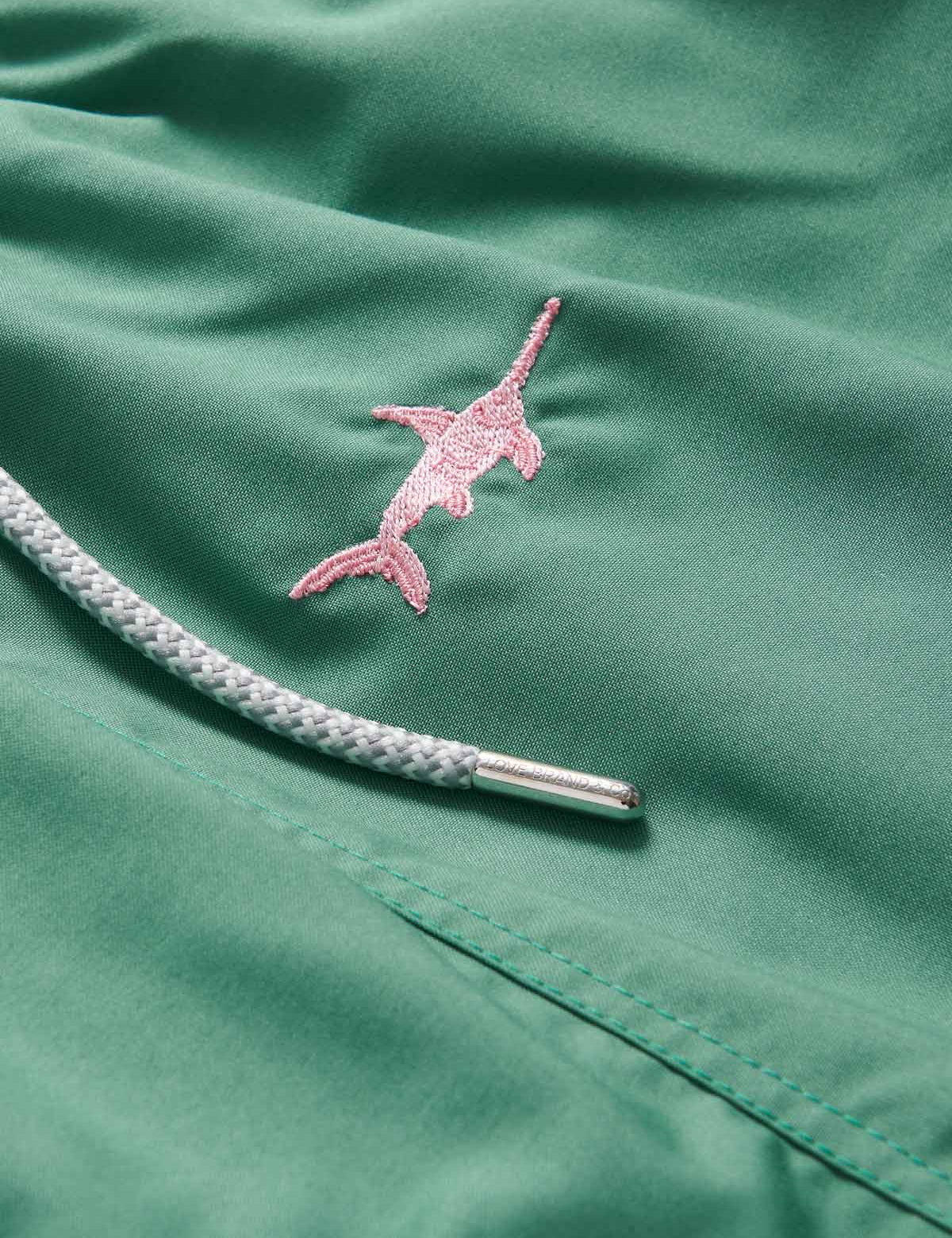 Close-up view of Men's Staniel Swim Shorts featuring pink swordfish embroidery on green fabric and braided drawstring.