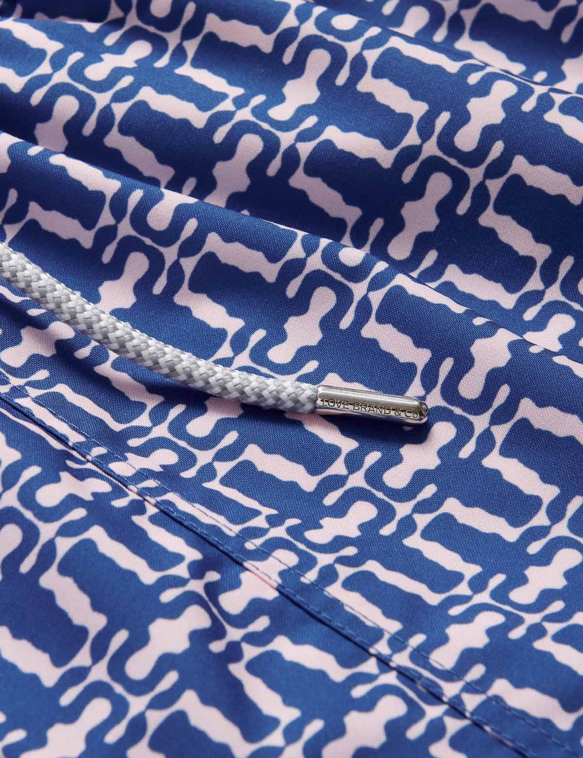 Close-up of Men's Wilderness Staniel Swim Shorts featuring a blue and white African-inspired geometric pattern with wildebeest horned heads and detailed drawstring.