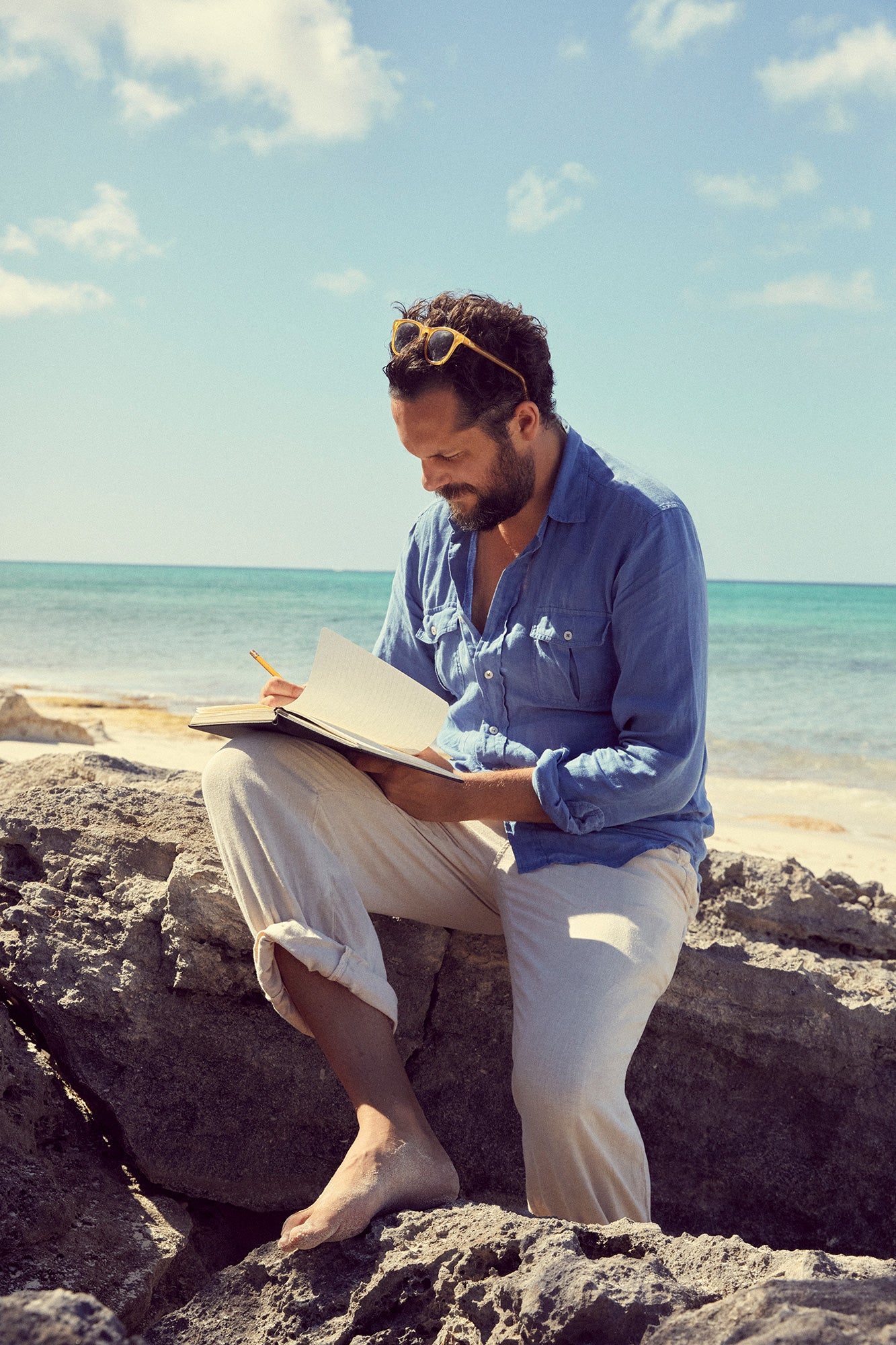Oliver Tomalin sitting on rocks by the ocean, writing in a notebook.