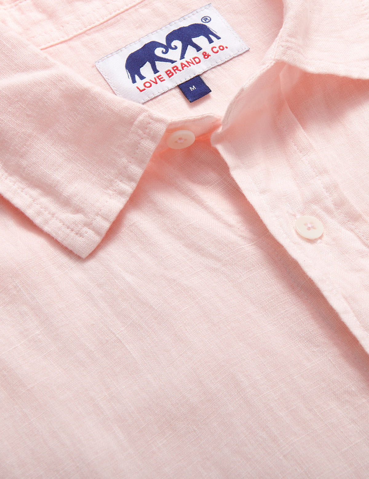 Pastel pink Manjack linen shirt for men, 100% linen, short-sleeved, lightweight, shown with detailed stitching and buttons.