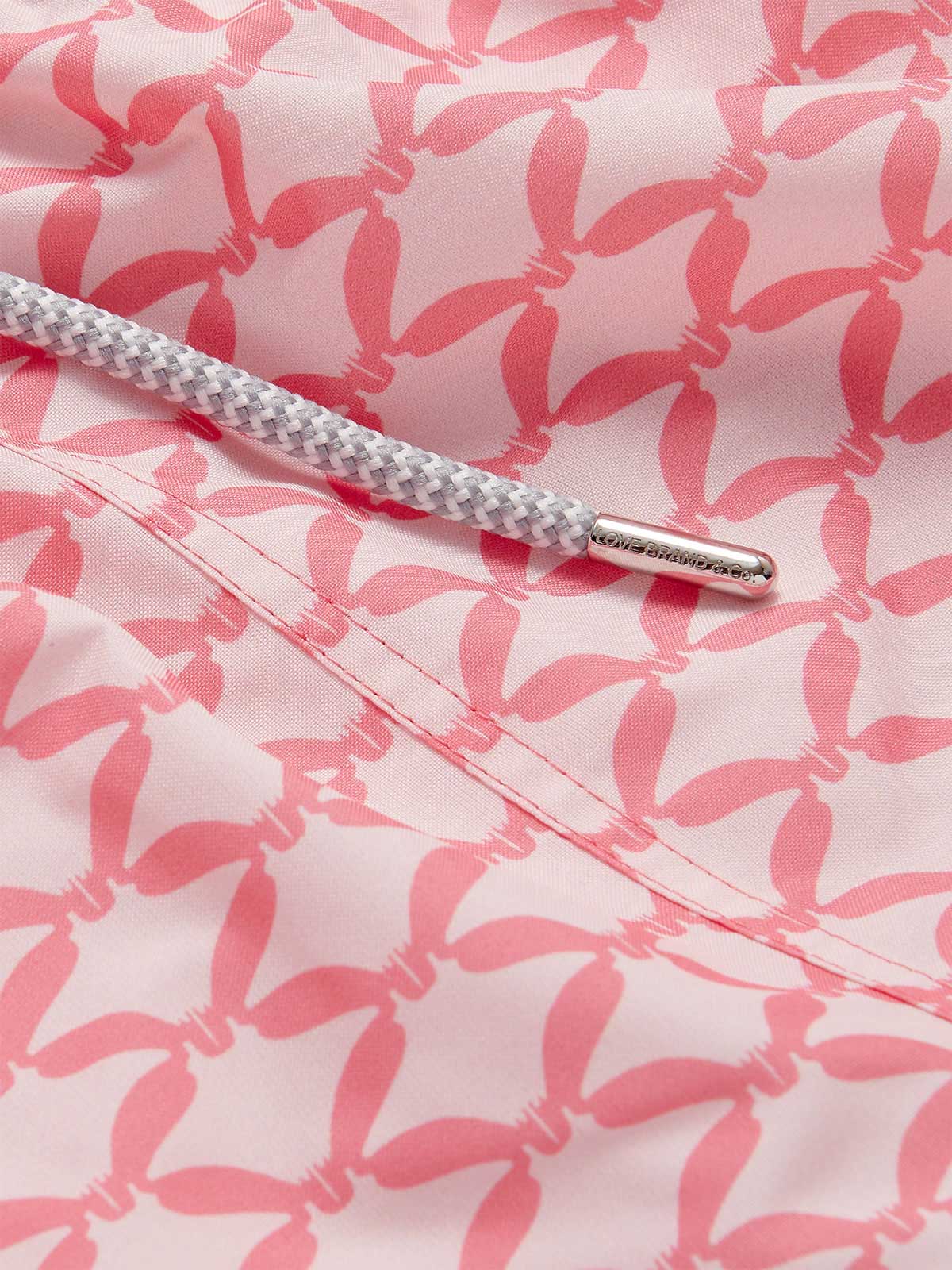 Close-up view of Men's Ray Rhythm Staniel Swim Shorts showcasing a distinct diamond geometric print. Patterned swim shorts with graceful manta rays in soothing watermelon and light pink hues, and a detailed braided drawstring.