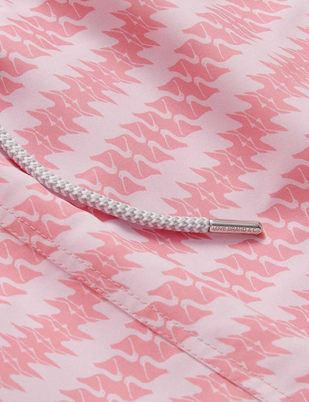 Close-up of the patterned fabric and drawstring detail of the Men's Roseate Spoonbill Staniel Swim Shorts. Patterned swim shorts showcasing a pink and white design inspired by the graceful motion of the roseate spoonbill. Made from 100% recycled, quick-drying fabric for comfort and style.