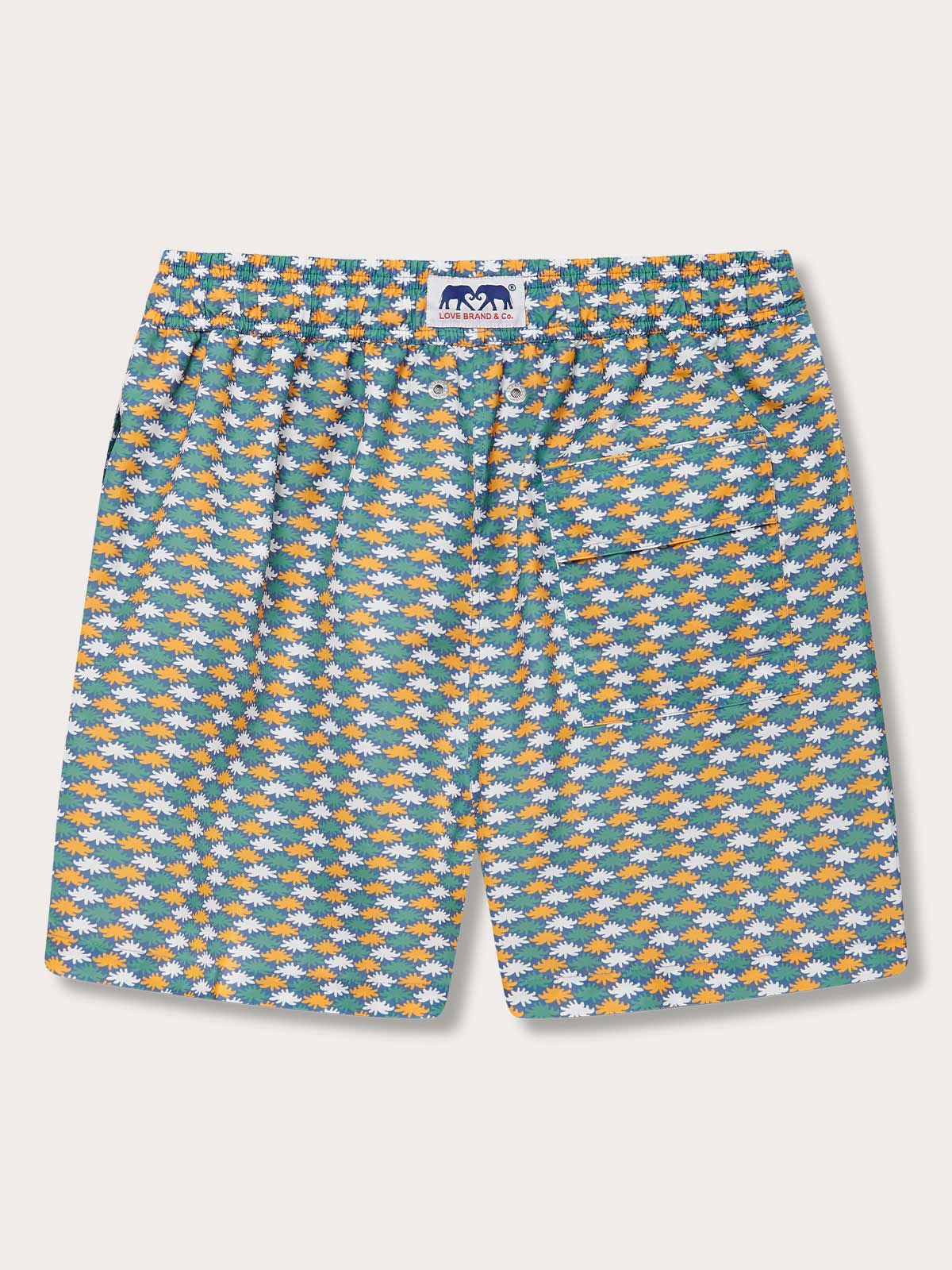 Men's Sea Flowers Staniel Swim Shorts with a vivid pattern of ochre, white, and green sea anemones. Patterned swim shorts on a deep blue background, made from 100% recycled materials.