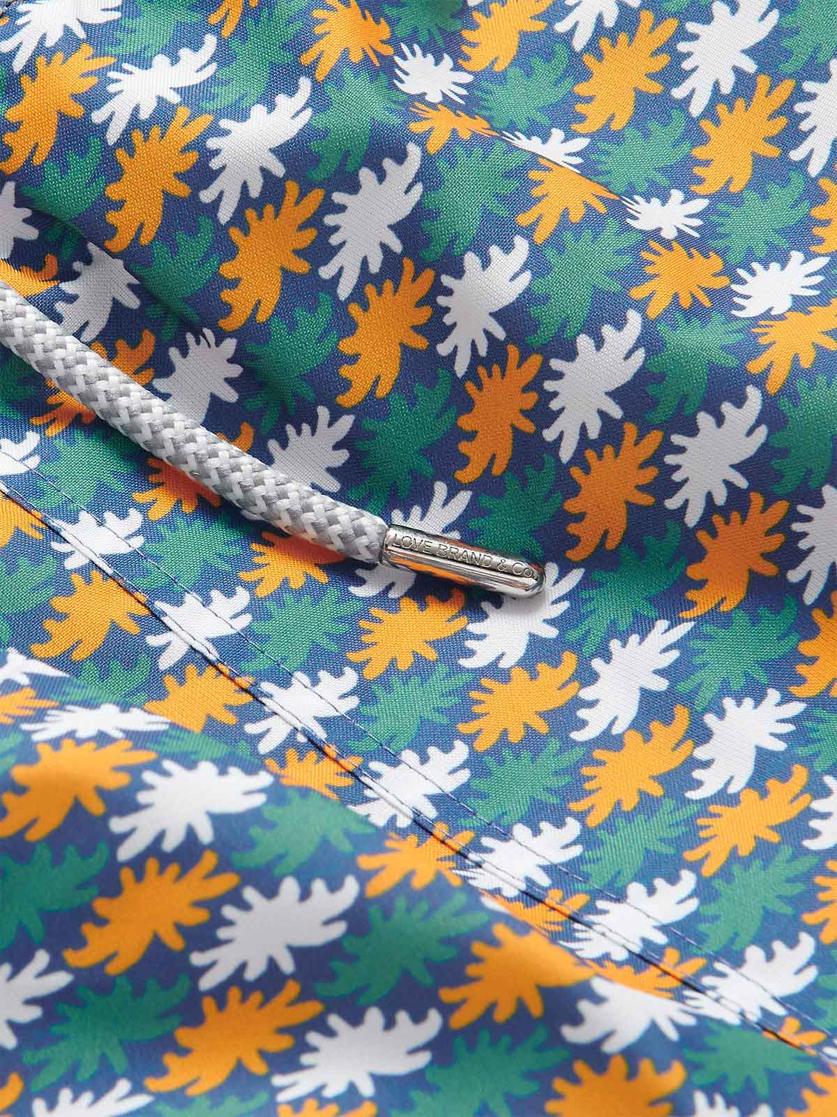 Close-up view of Men's Sea Flowers Staniel Swim Shorts featuring a pattern of ochre, white, and green sea anemones on a deep blue background, with a detailed braided drawstring.