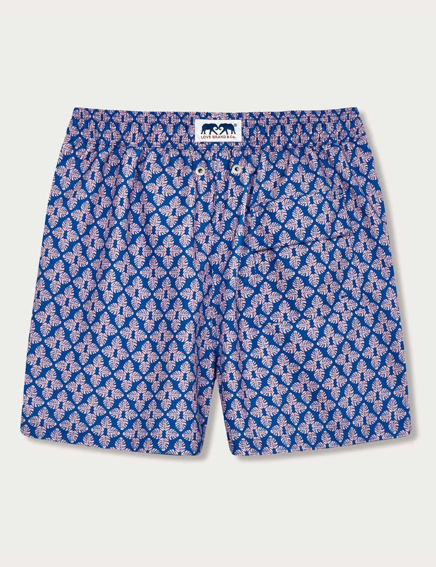 Men's Palm Paradise Staniel Swim Shorts. Patterned swim shorts with pastel pink Monstera leaf print on blue background.