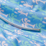 Close-up of Men's Party Like a LobStar Staniel Swim Shorts featuring a pattern of dancing lobsters and swaying palm trees on a blue background with a white drawstring.