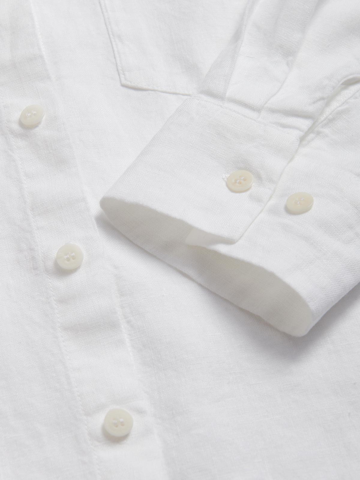 Detailed view of the cuffs of Womens White Inagua Linen Shirt. Long-sleeved button-up plain linen shirt with front pocket. Cuffs showing sustainable corozo nut button fastening.