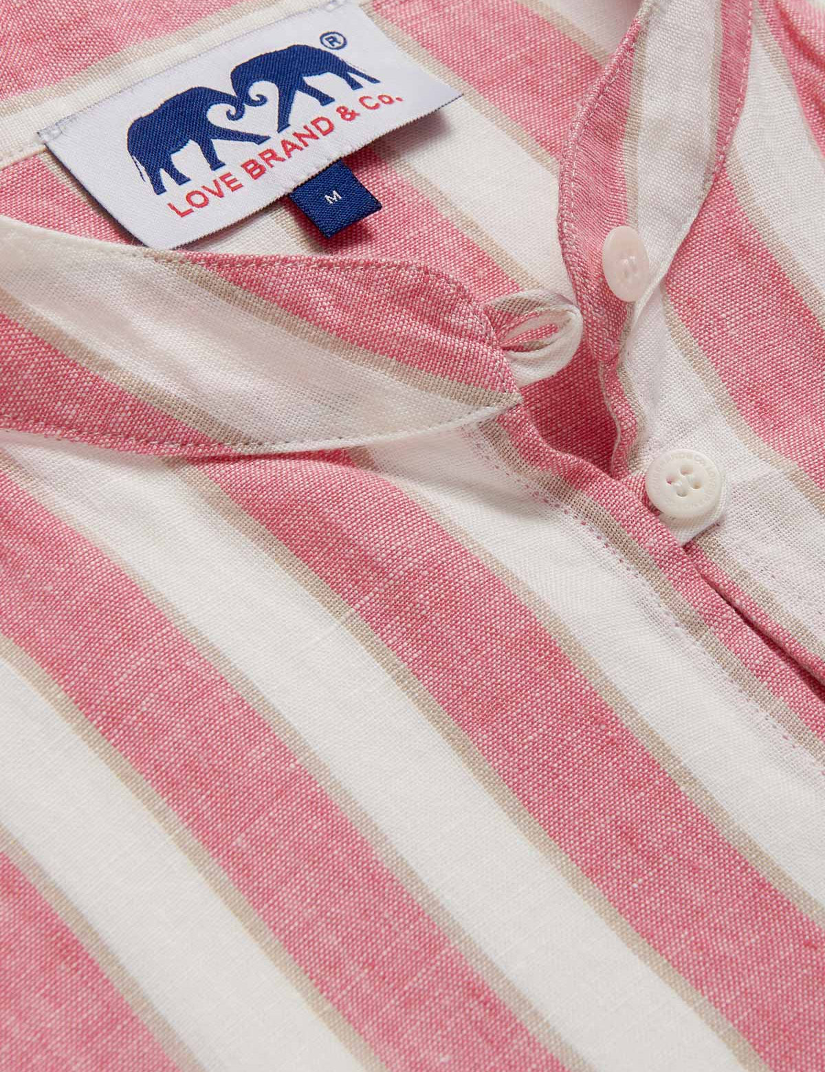 Detailed view of Womens Strawberries & Cream Jumento Linen Poncho. Half-button up, short-sleeved linen poncho in a white and pink striped pattern. Picture showcases white corozo nut buttons and love brand label.