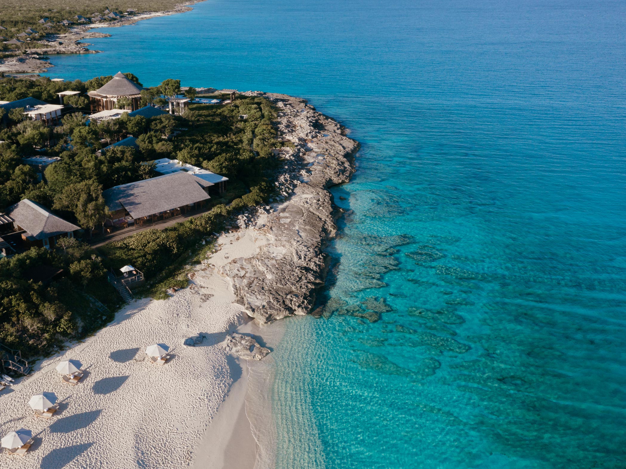 Aerial view of Amanyara beach with clear blue water and a rocky shoreline.