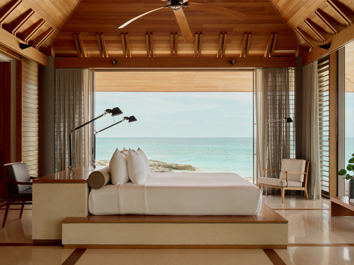 Modern bedroom with ocean view, wooden ceiling, and large windows.