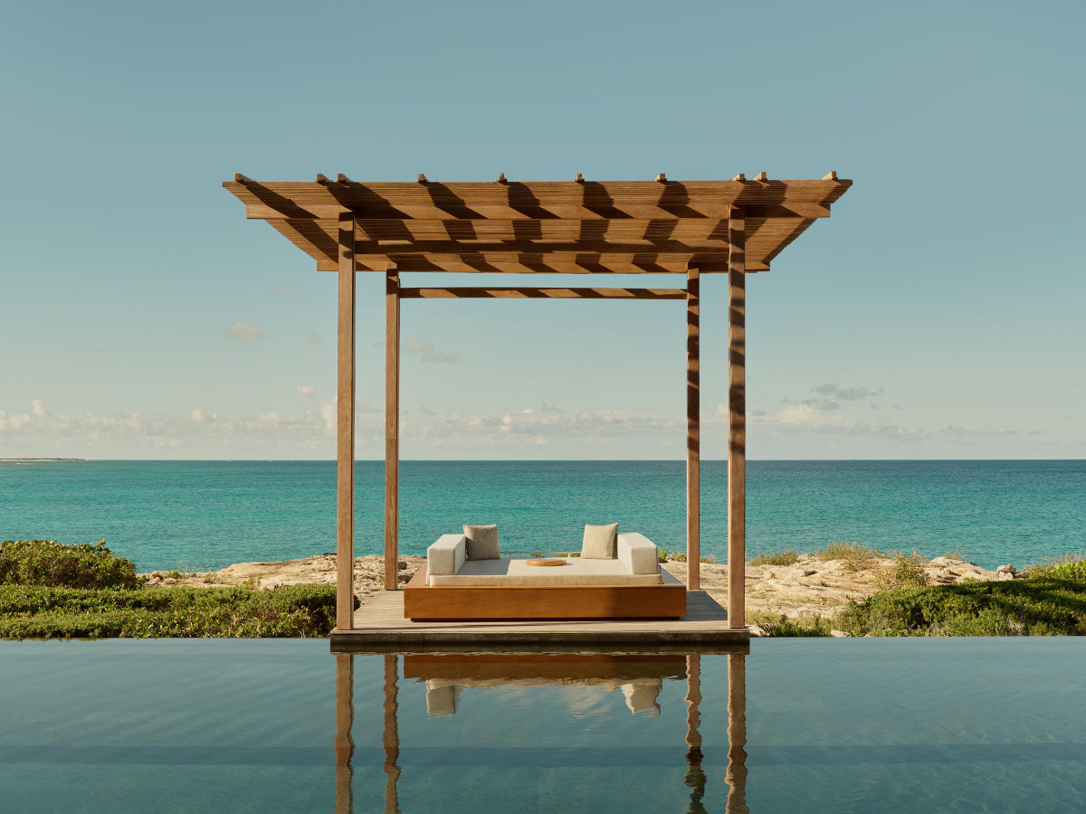Wooden pergola with lounge chairs by a pool overlooking the ocean.