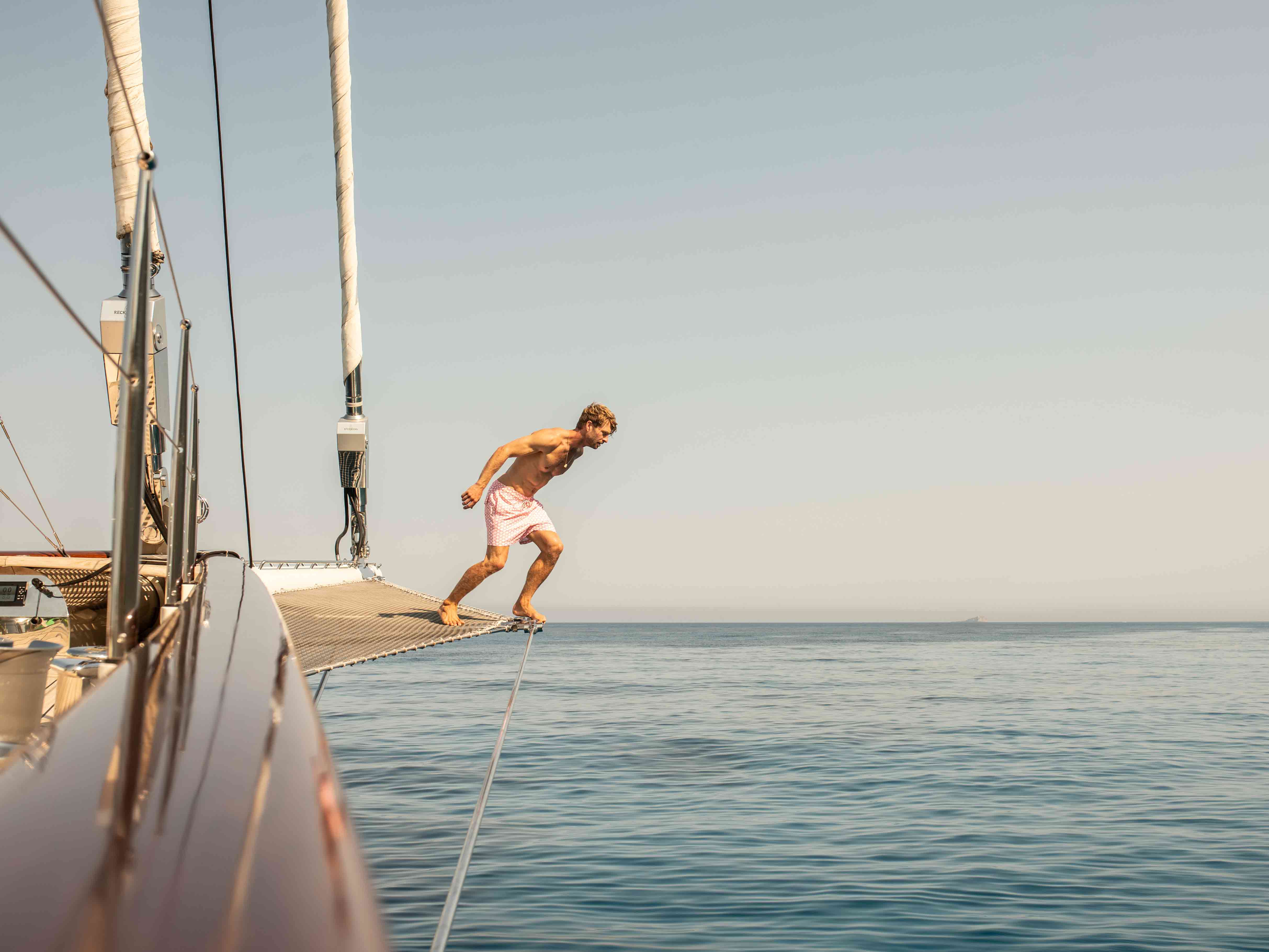 man wearing love brand red and white swim shorts jumps into ocean from luxury yacht athos