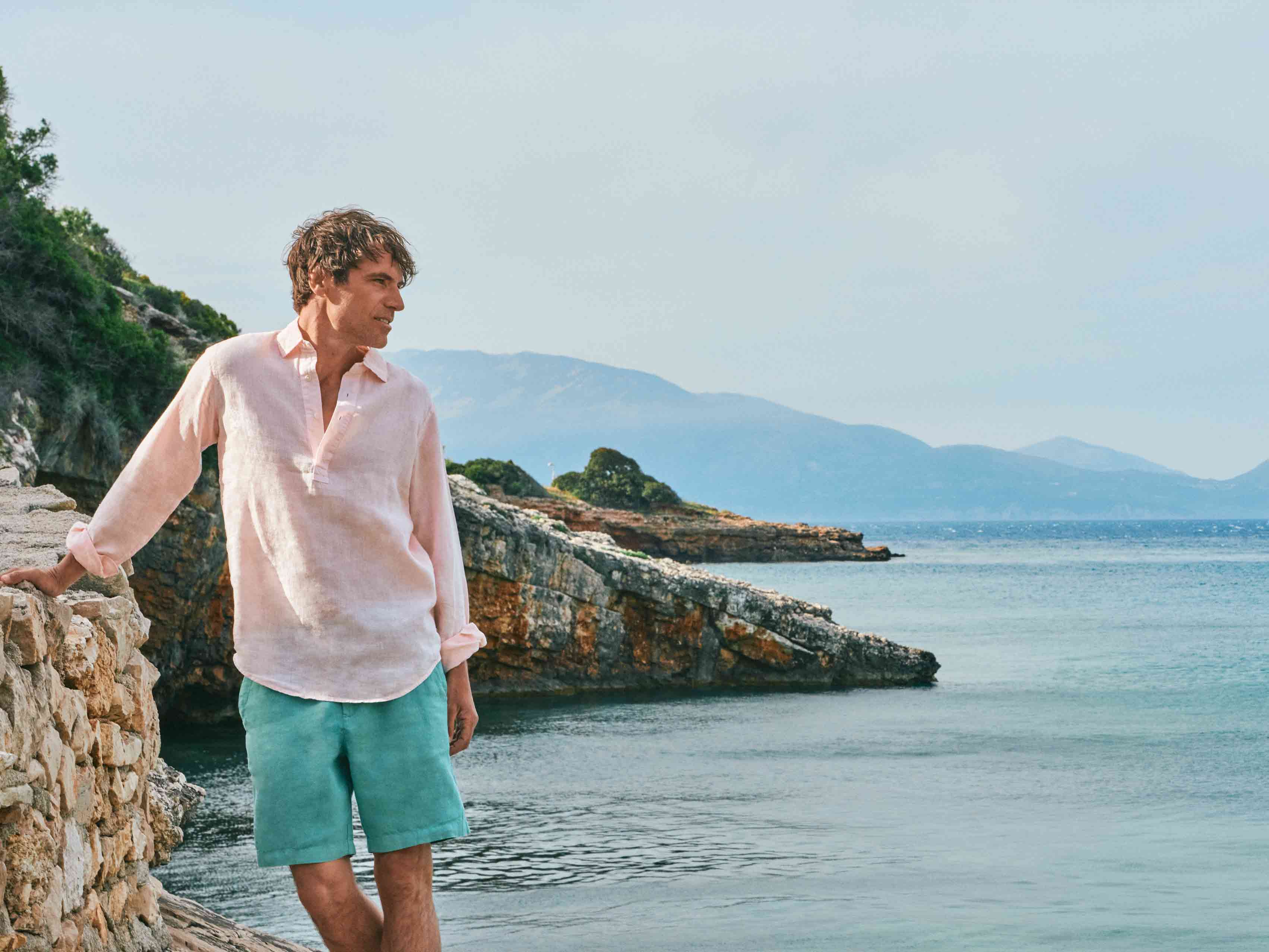 man wears pastel pink linen shirt with a backdrop of the French riviera