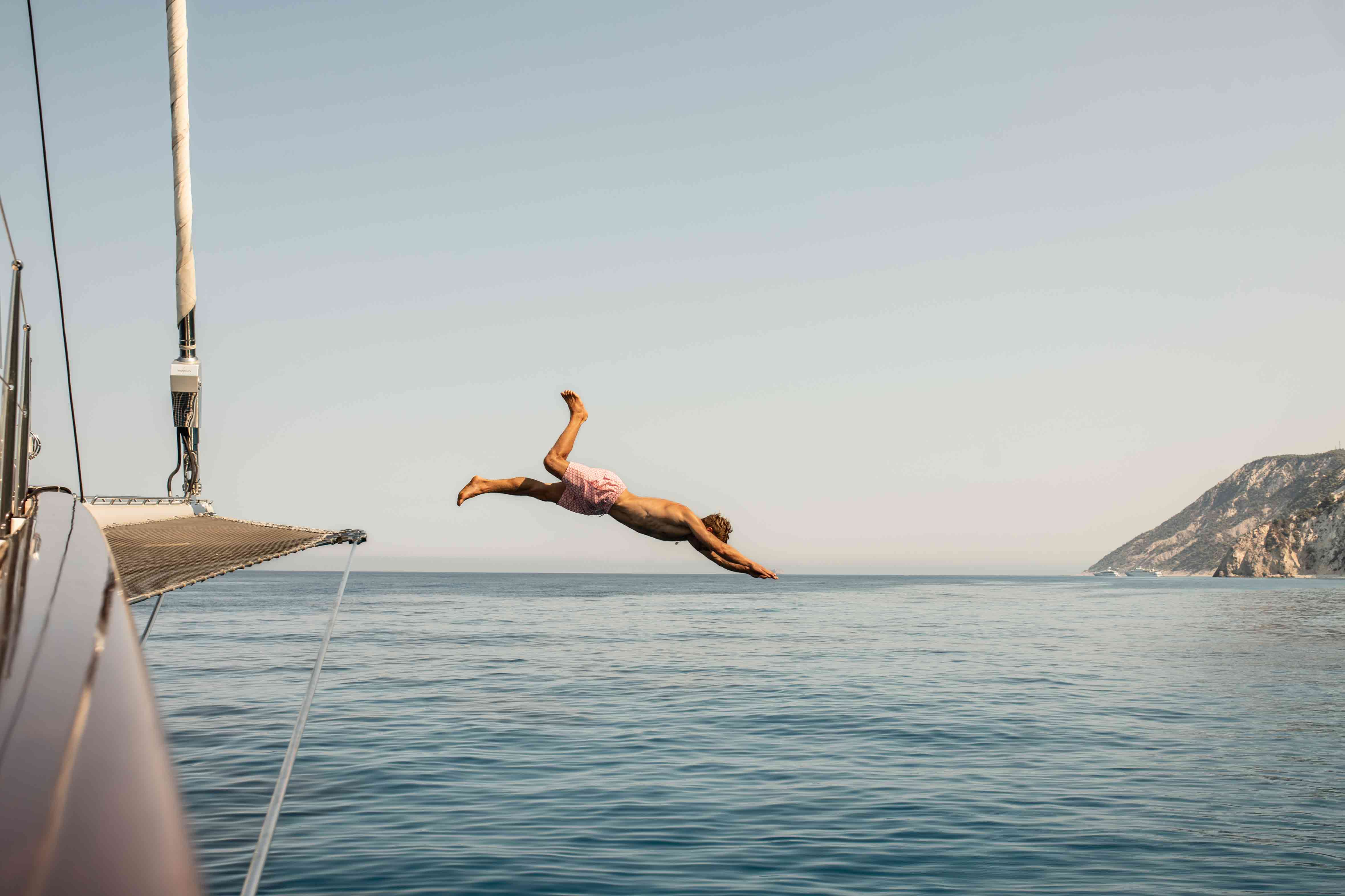 man wearing love brand red swimming shorts jumps from athos yacht into ocean