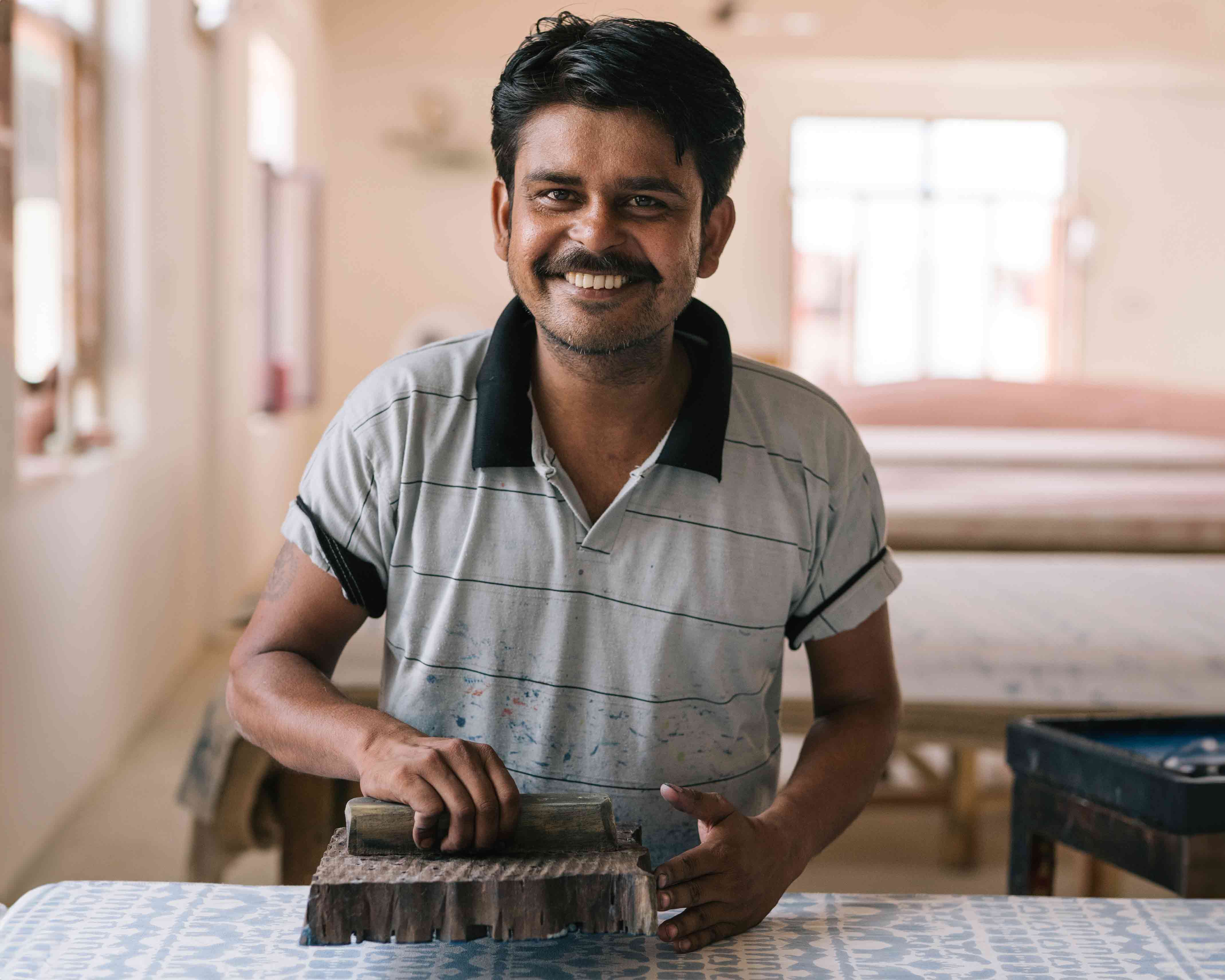 Love Brand & co. artisan creating the Coexist print using tradiitonal block printing techniques. He ispictured using a hand-made wooden block dipped in blue dye to transfer the blue print onto the white fabric.