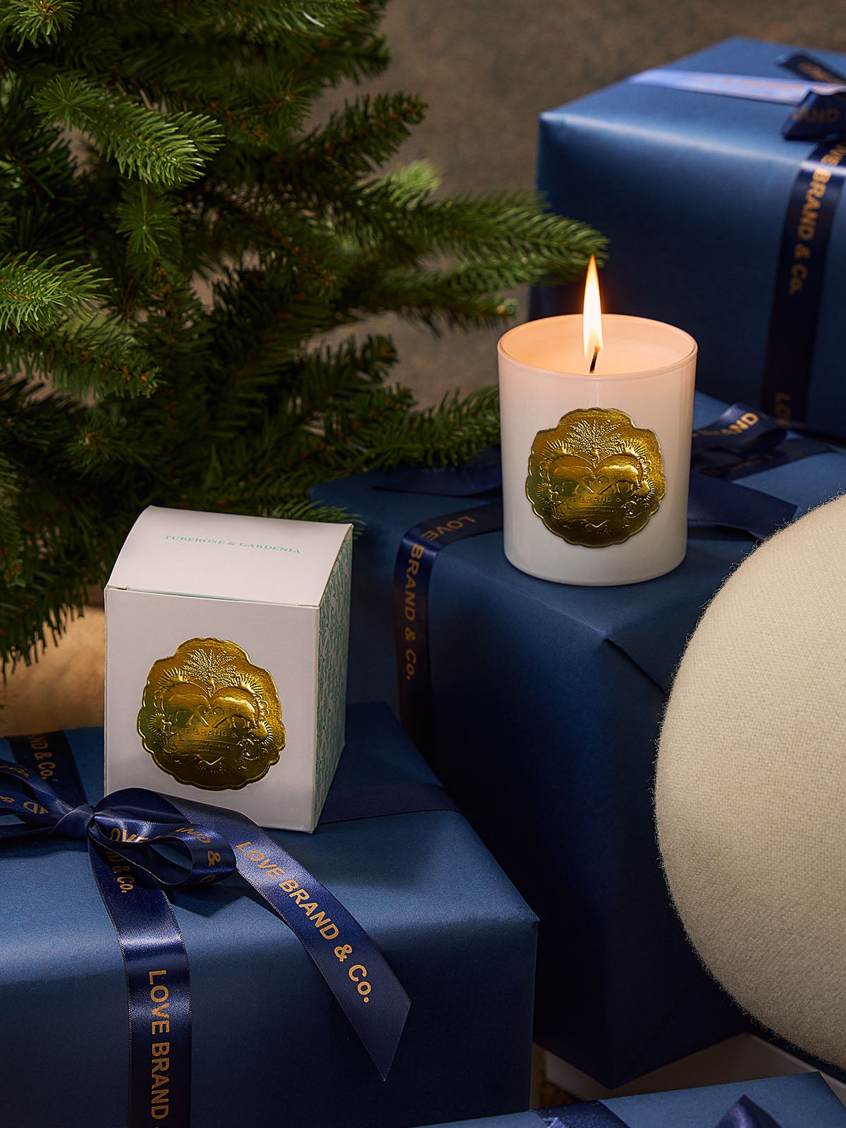 Candle with a decorative elephant emblem on a blue gift box next to a Christmas tree.