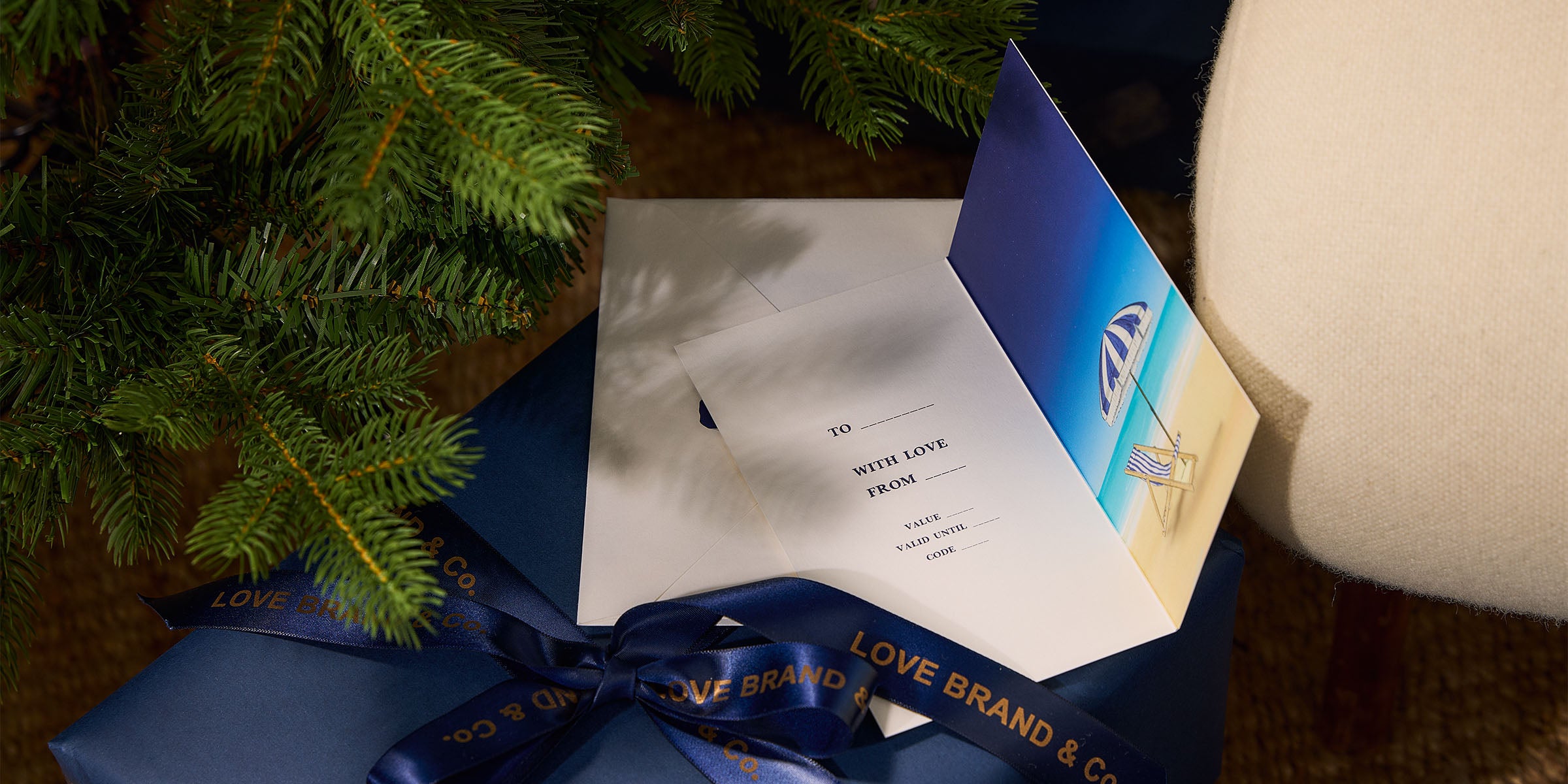 Greeting card with blue envelope and ribbon next to a Christmas tree