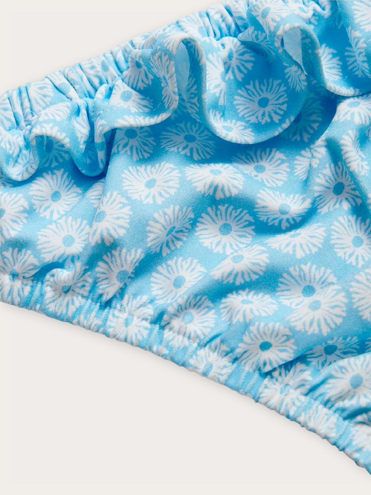 A close-up of a light blue ruffled fabric trim with a white floral pattern, shown against a plain off-white background.