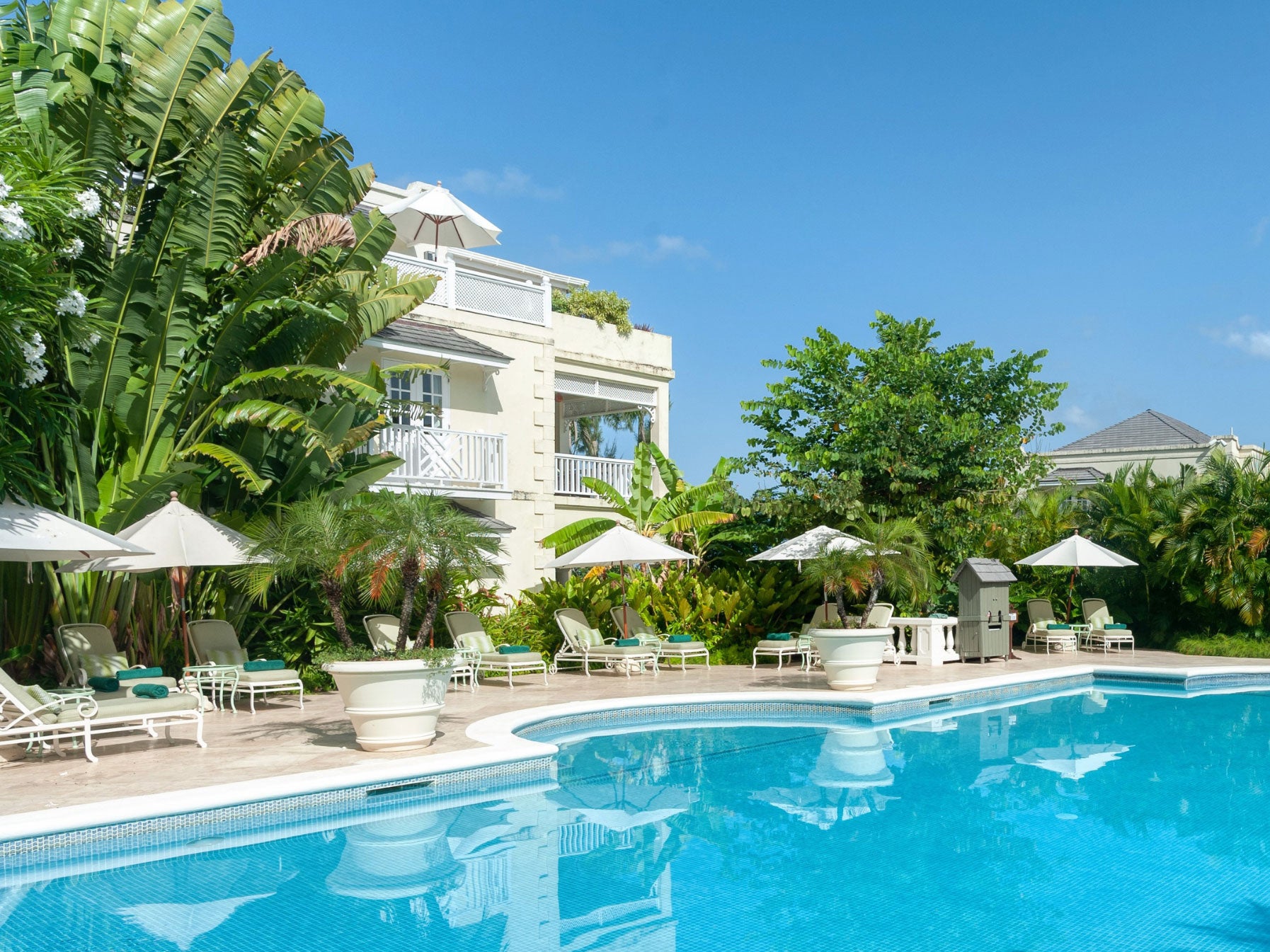 Pool area with lounge chairs, umbrellas, and a building in the background