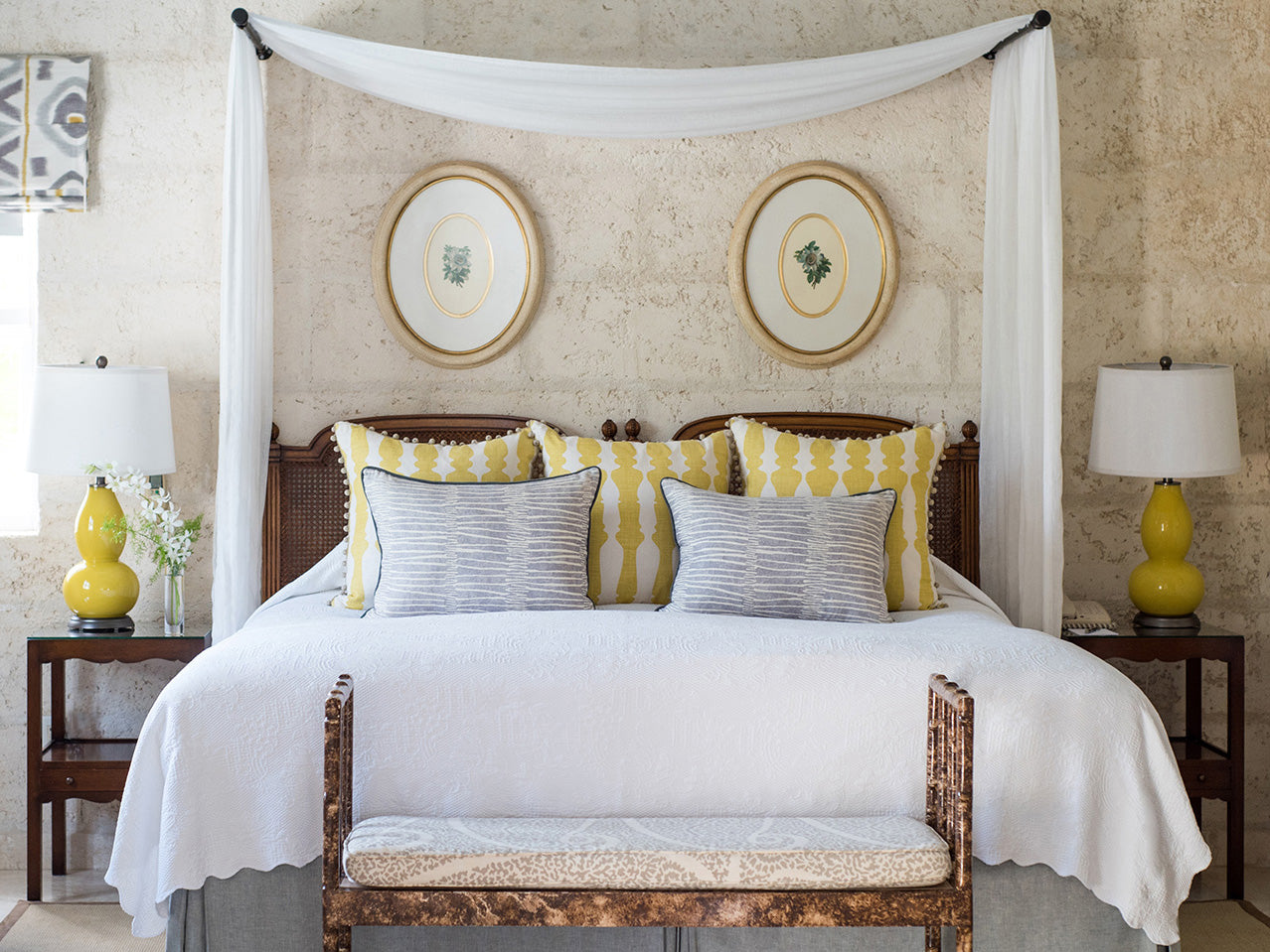 Bedroom at the Coral Reef Club with a canopy bed, yellow and grey striped pillows, and decorative lamps.