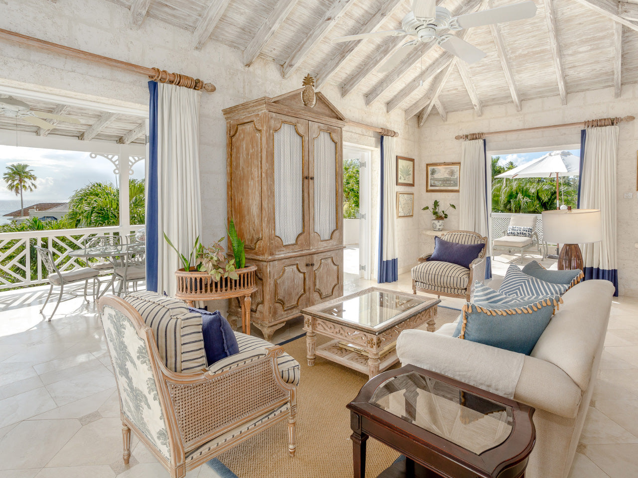Living room area of Coral Reef Club accommodation with white walls, wooden furniture, and large windows.