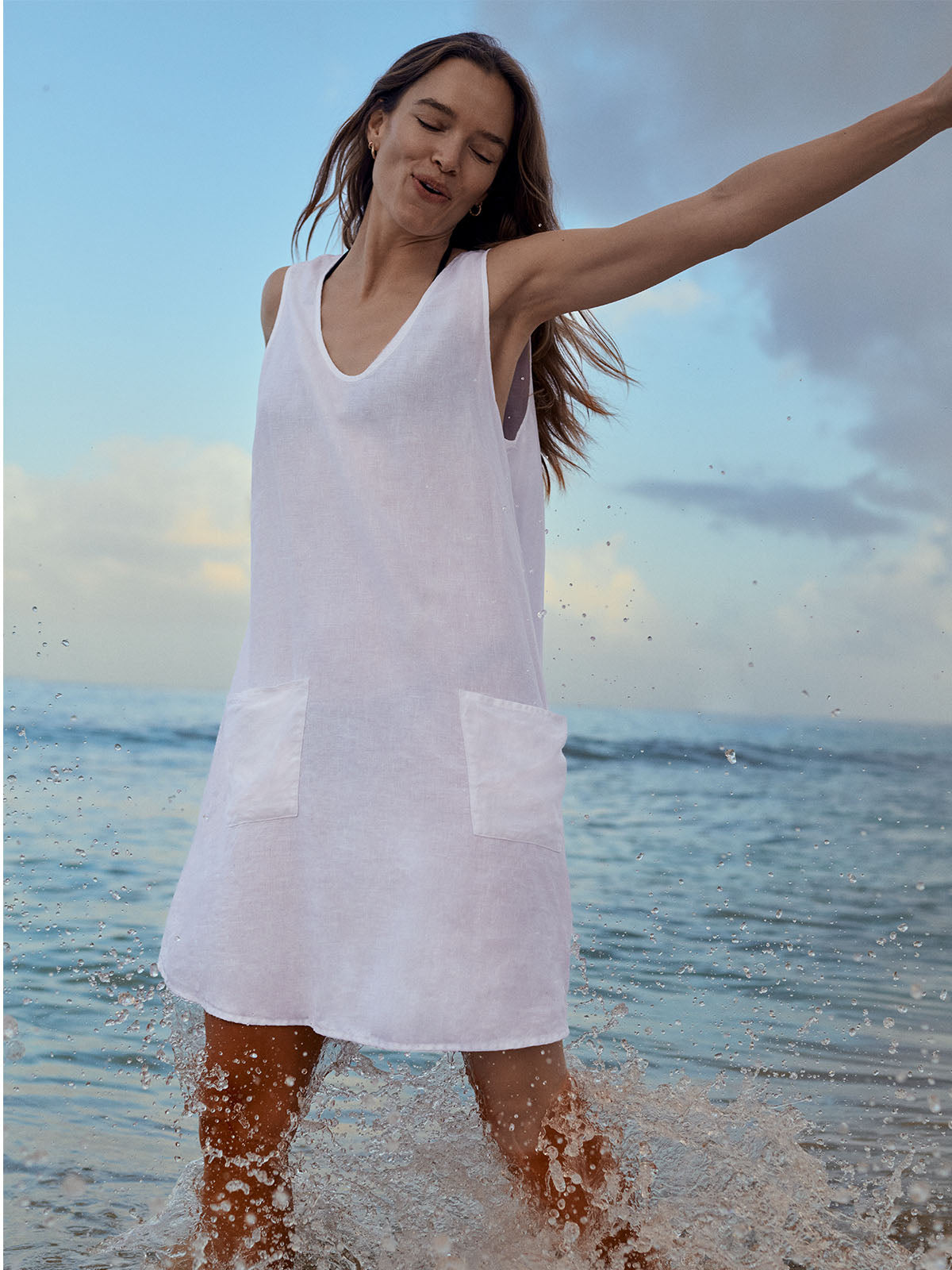 Woman in a white dress standing in shallow water with a blue sky and ocean background
