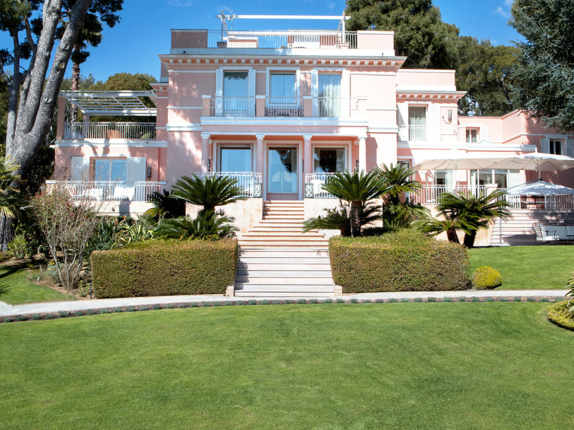 Luxurious pink mansion at Four Seasons with a well-manicured lawn and palm trees.