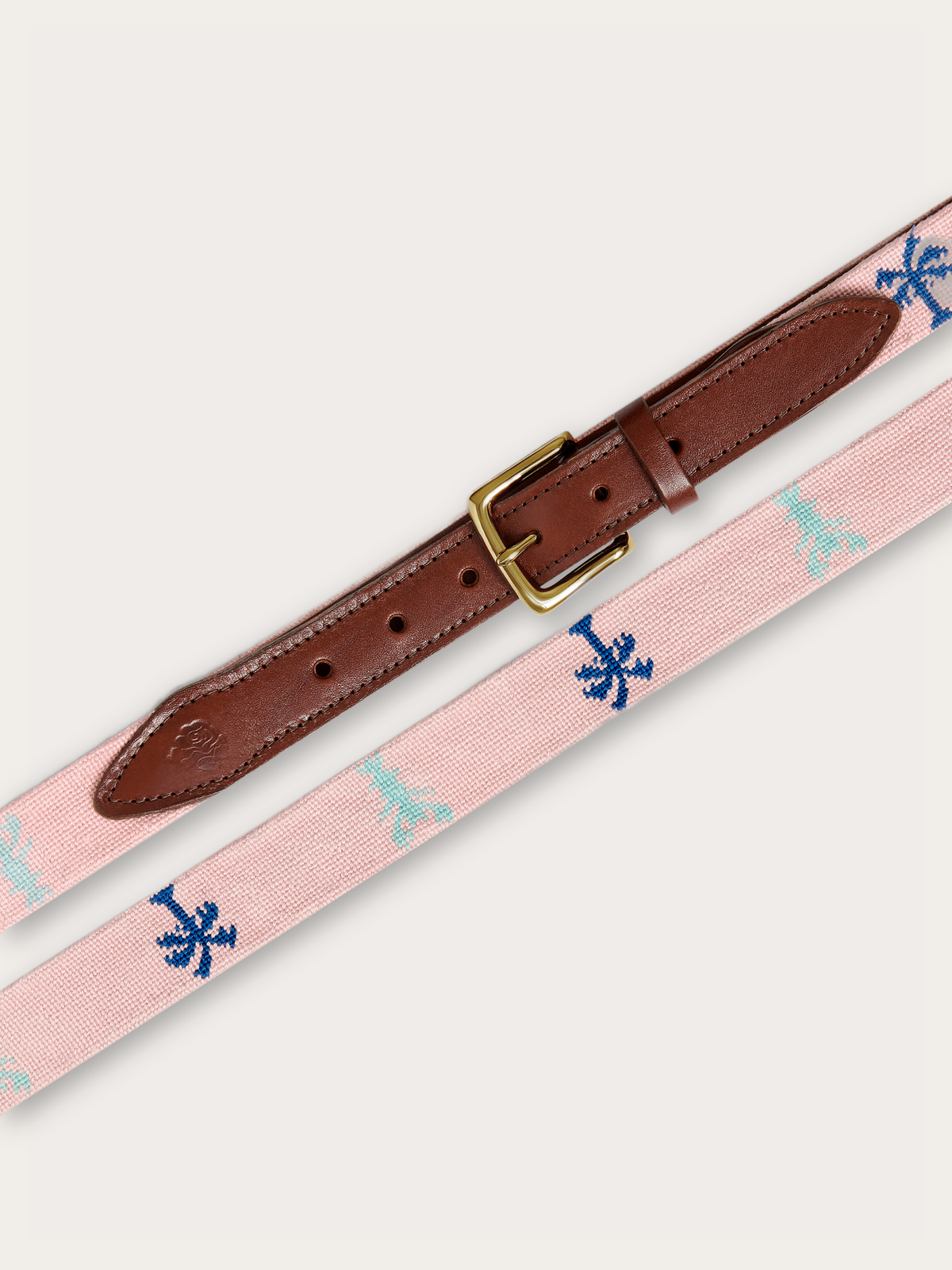 A pink woven belt with a brown leather end and a gold-tone buckle, featuring a repeating embroidered logo pattern in blue and light blue on a light grey background.
