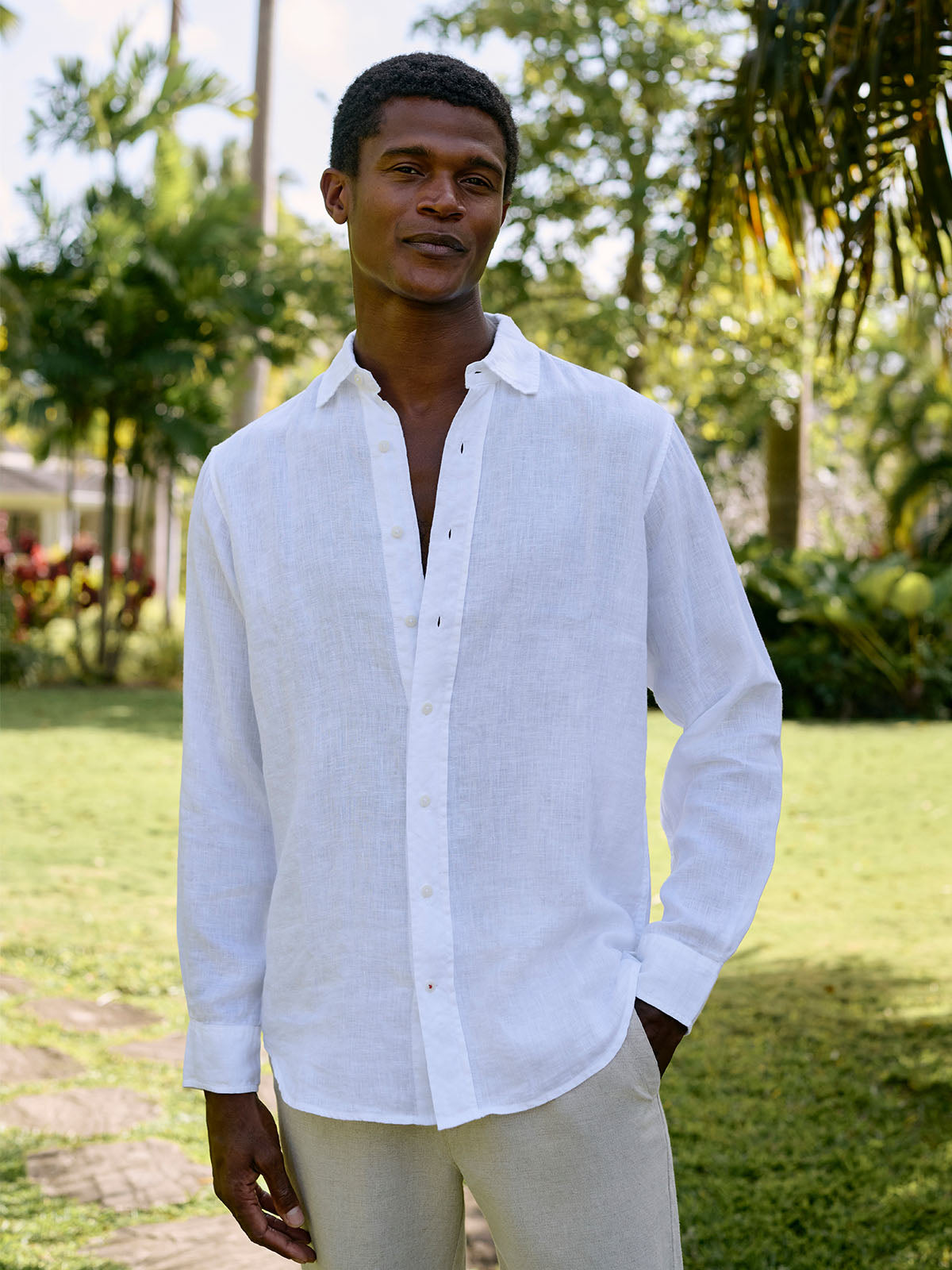 Man wearing a white linen shirt standing outdoors with greenery in the background