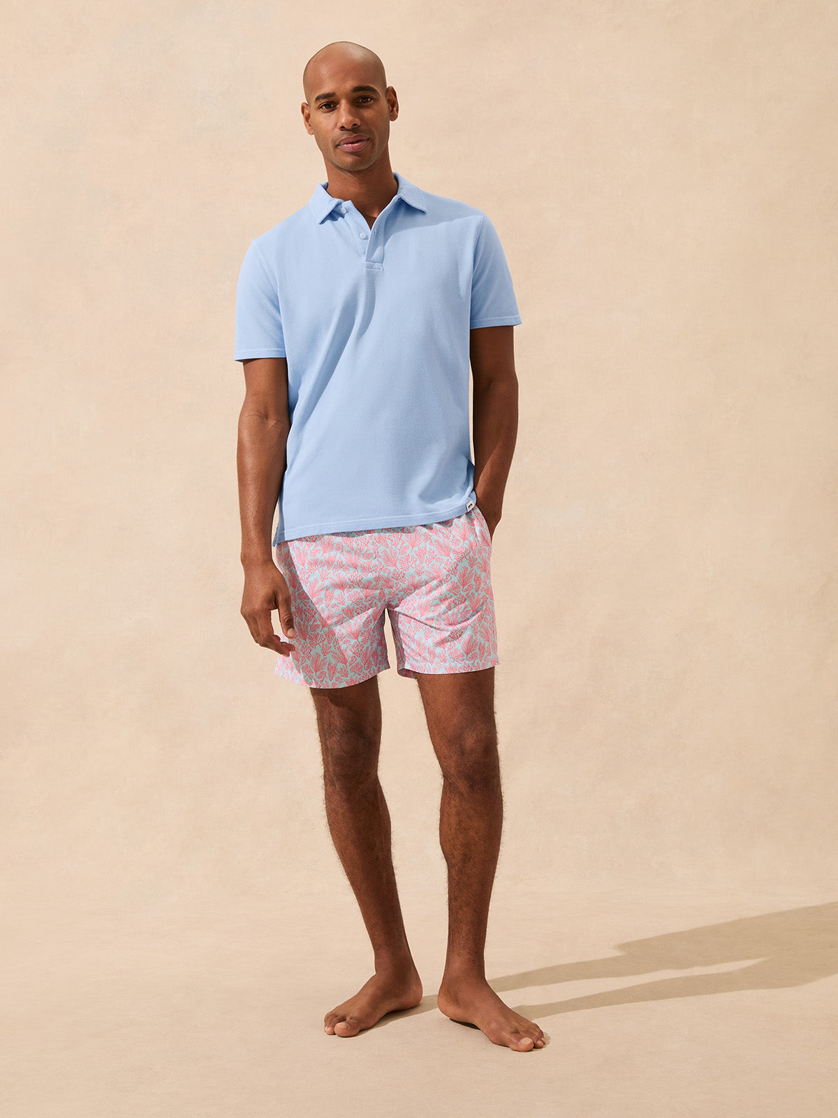 Man wears a light blue polo shirt paired with light blue and pink swim shorts with a coral pattern