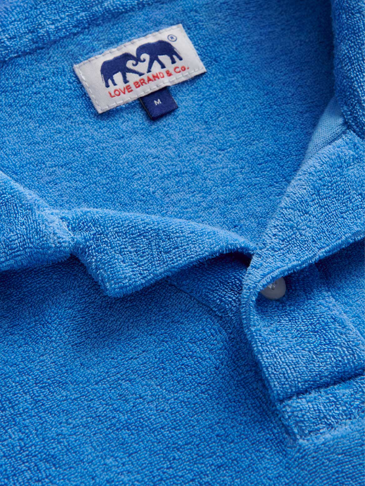close-up of blue terry polo shirt showing love brand logo label.