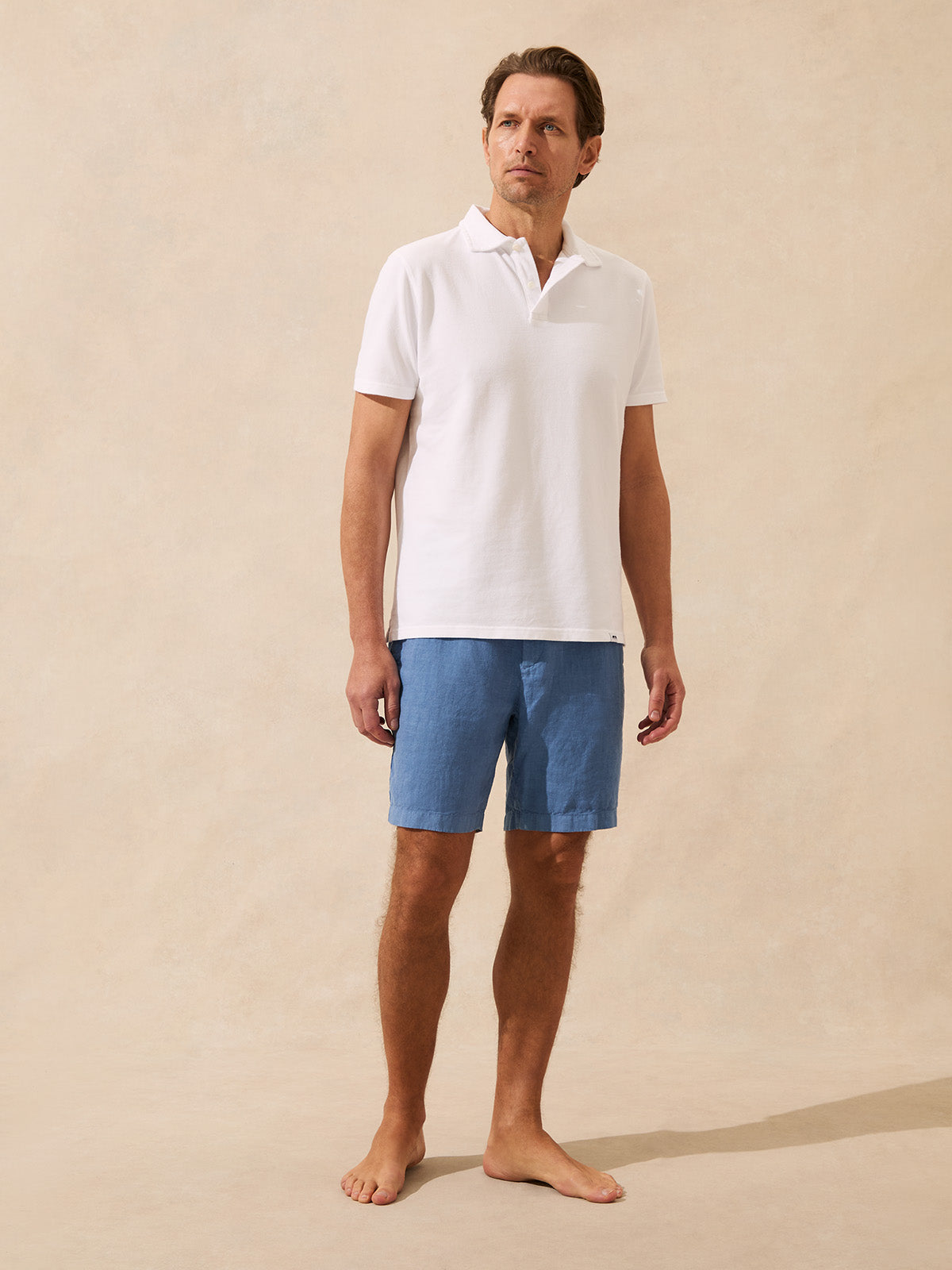 Man wearing a white polo shirt and blue shorts on a beige background