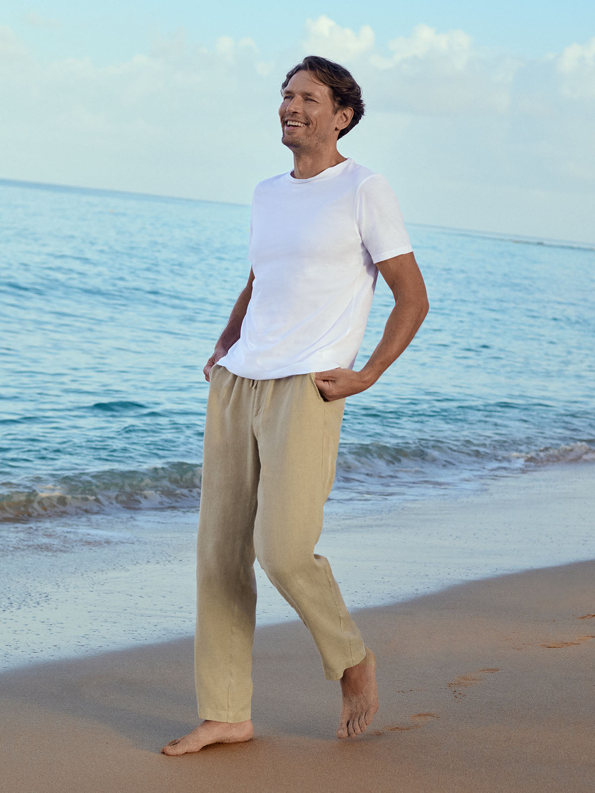Man standing on a beach wearing a white t-shirt and beige pants.